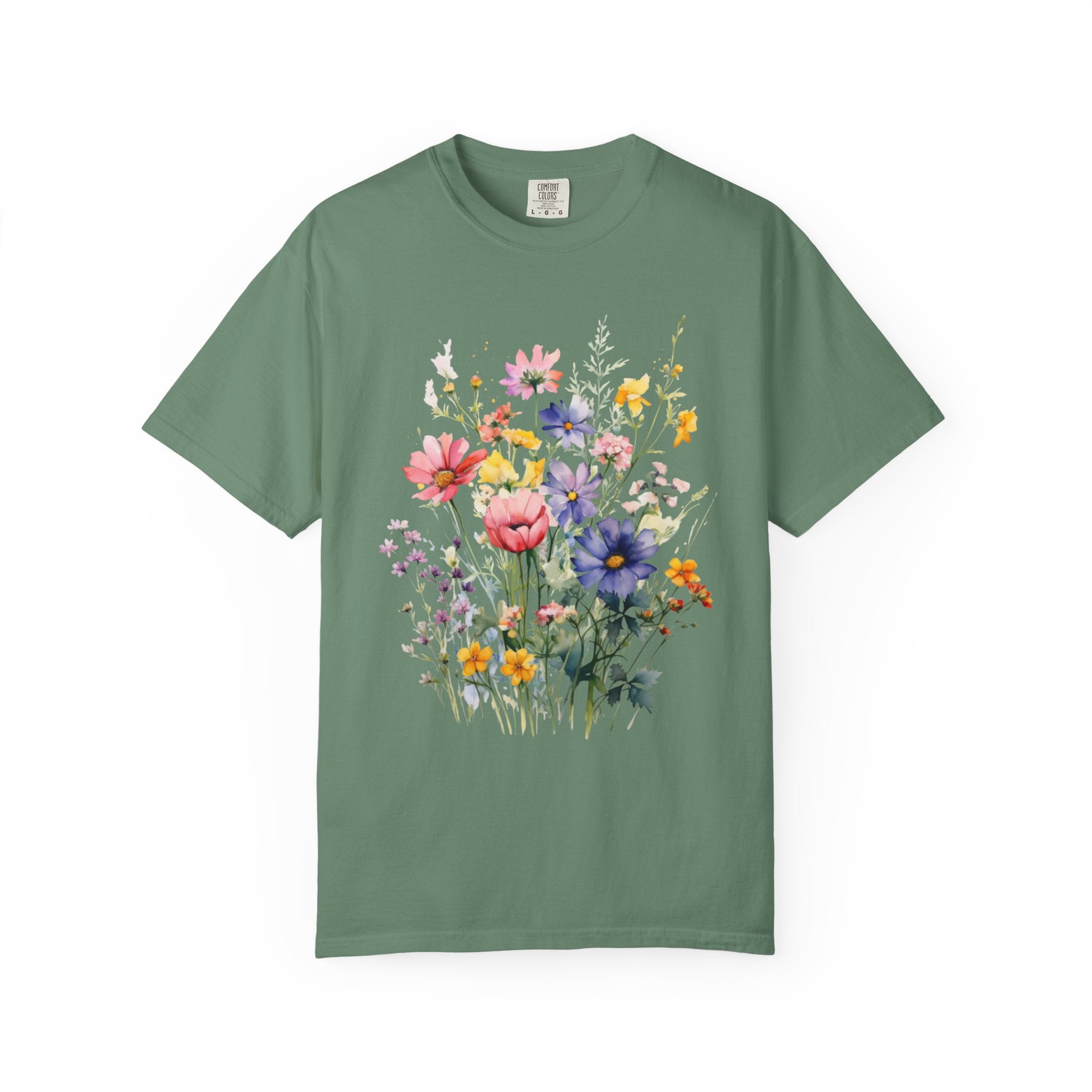 Watercolor-style wildflower meadow illustration with soft pink, yellow, blue, and lavender flowers on green stems, printed on a Comfort Colors shirt.