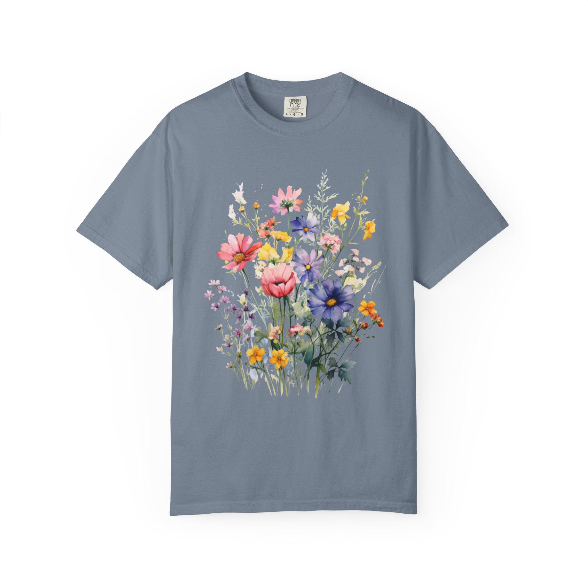 Watercolor-style wildflower meadow illustration with soft pink, yellow, blue, and lavender flowers on green stems, printed on a Comfort Colors shirt.