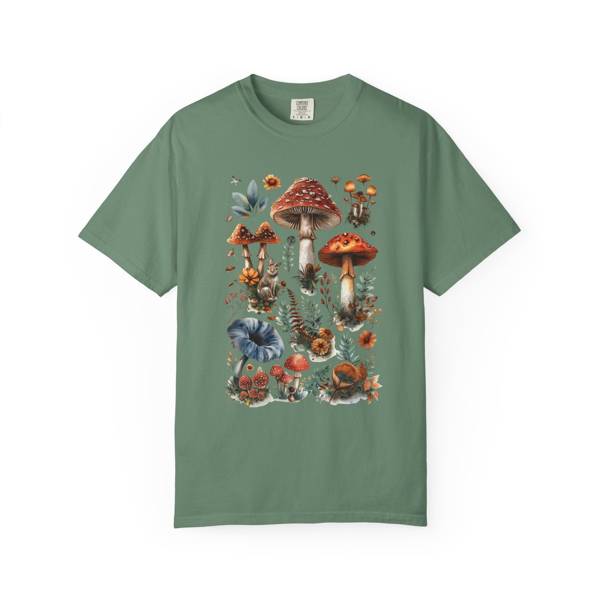 Illustrated woodland collage featuring red and brown mushrooms, leaves, flowers, and forest details in a vintage watercolor style, printed on a Comfort Colors shirt.