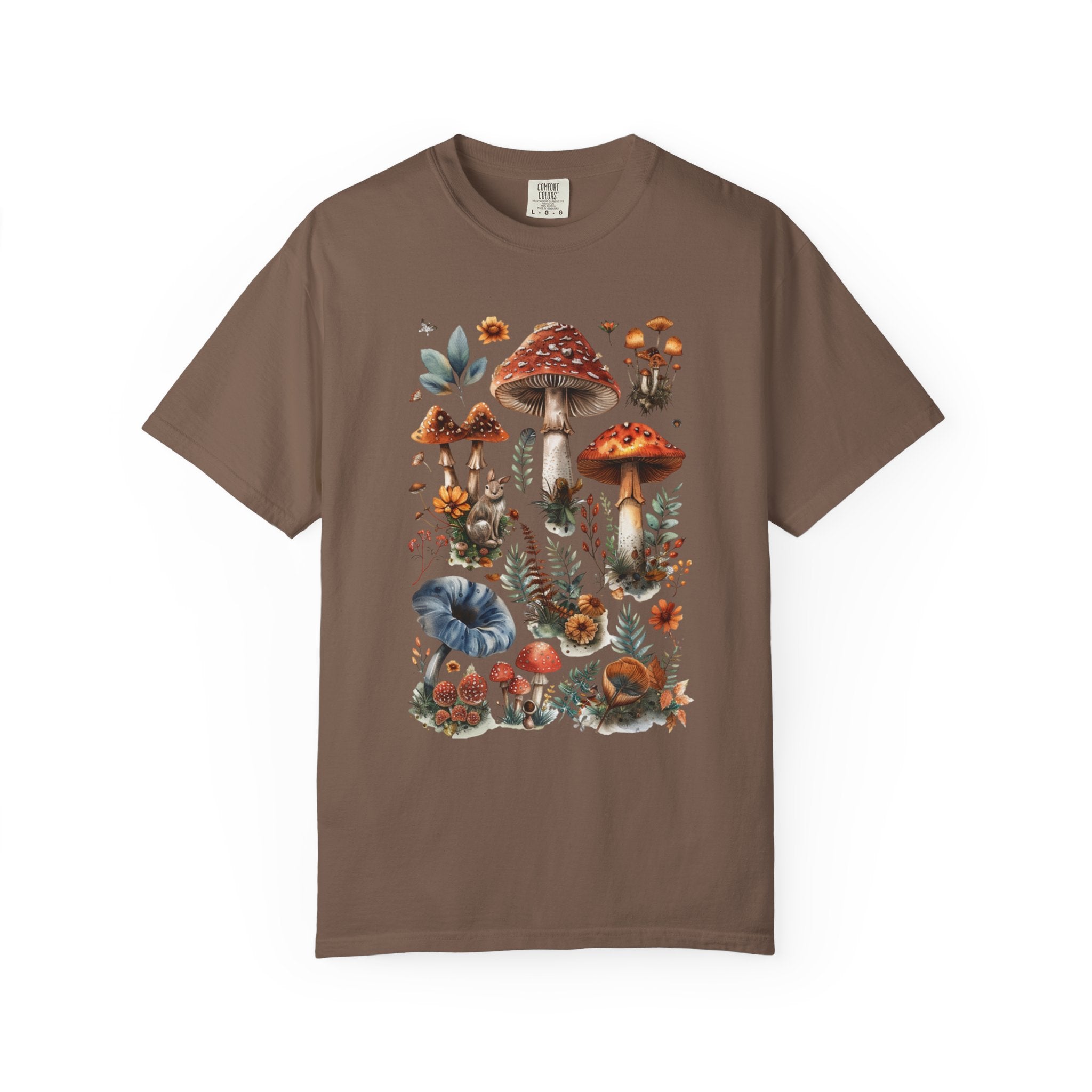 Illustrated woodland collage featuring red and brown mushrooms, leaves, flowers, and forest details in a vintage watercolor style, printed on a Comfort Colors shirt.