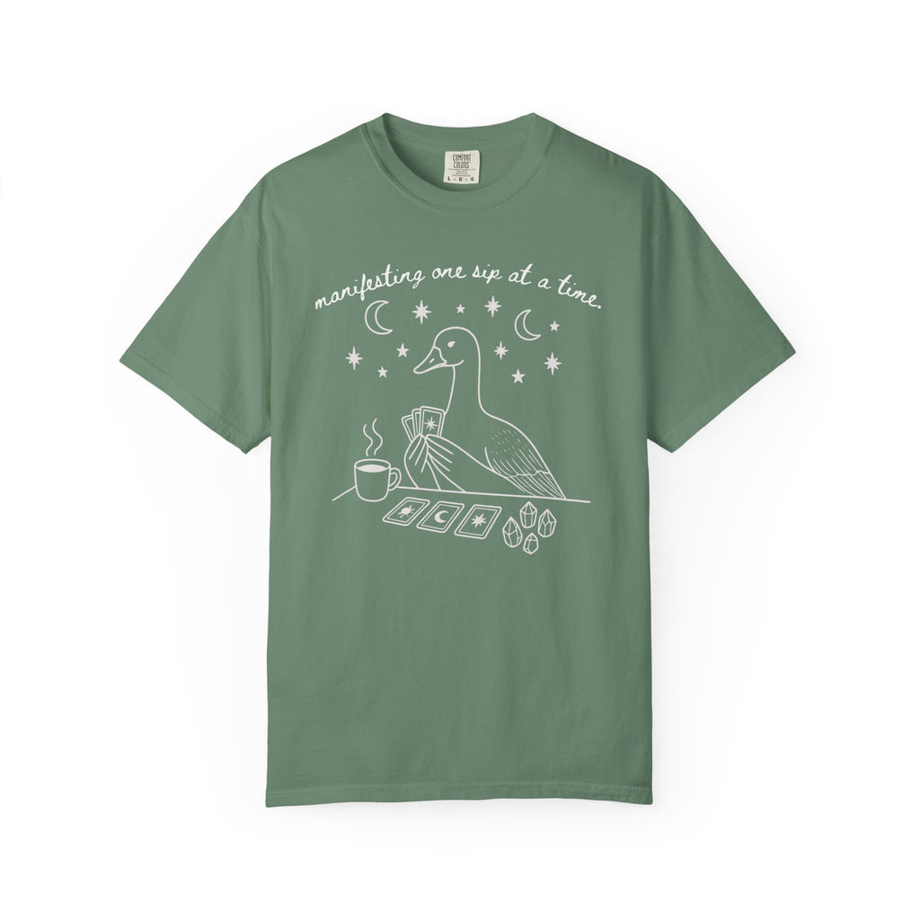 Comfort Colors t-shirt featuring a white tarot goose graphic with coffee, crystals, tarot cards, and the phrase "Manifesting One Sip at a Time."