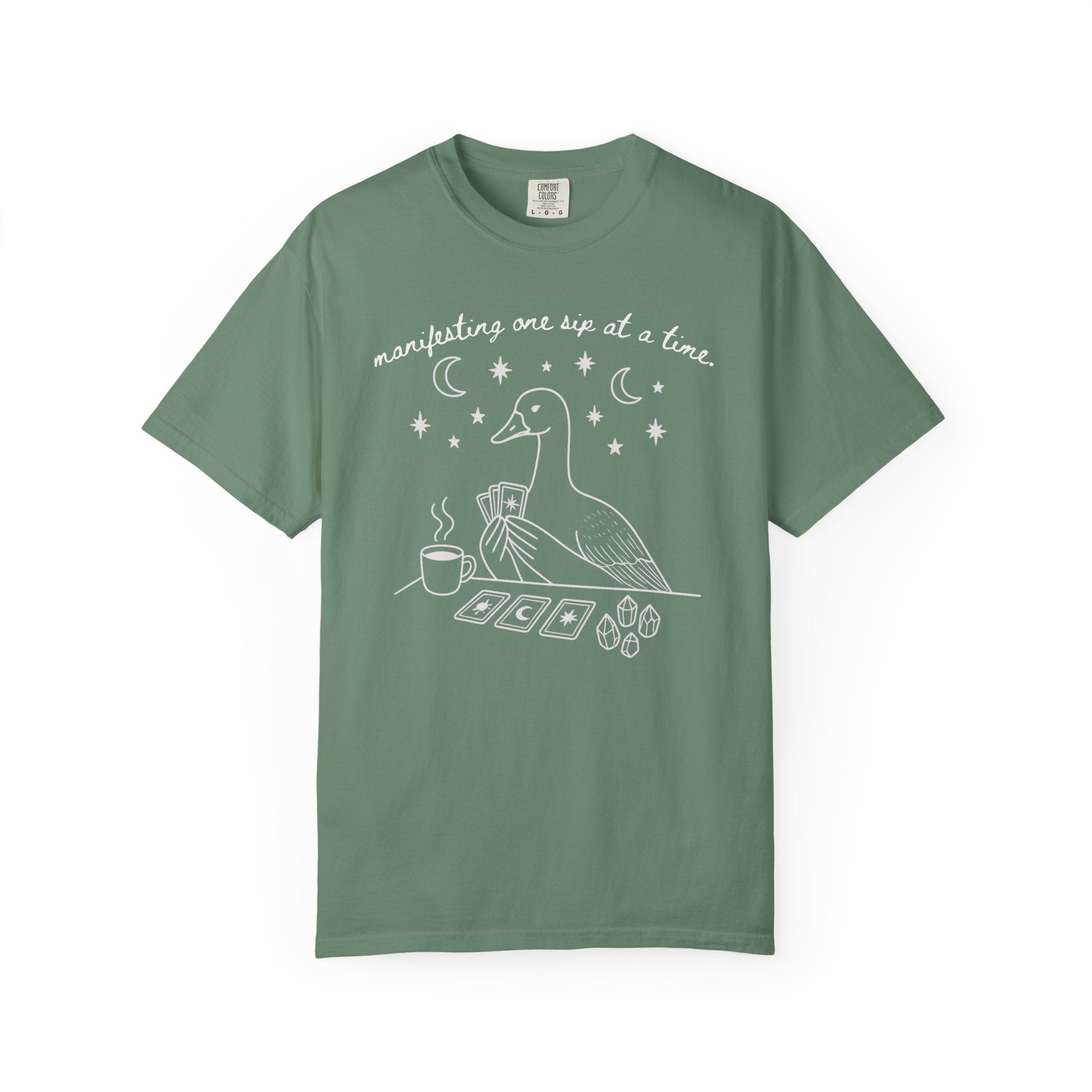 Comfort Colors t-shirt featuring a white tarot goose graphic with coffee, crystals, tarot cards, and the phrase "Manifesting One Sip at a Time."