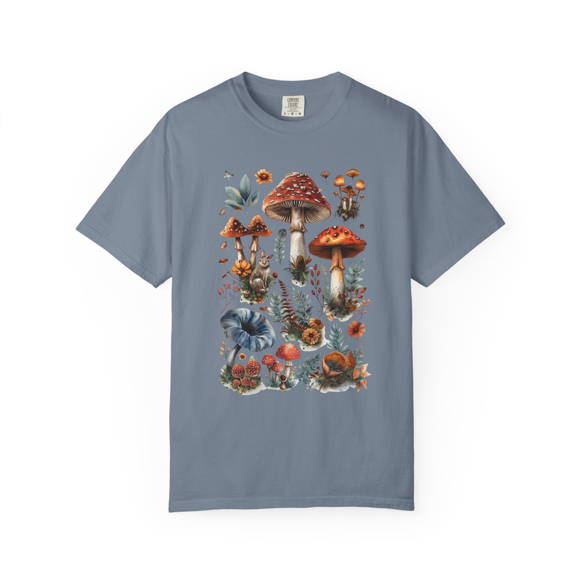 Illustrated woodland collage featuring red and brown mushrooms, leaves, flowers, and forest details in a vintage watercolor style, printed on a Comfort Colors shirt.
