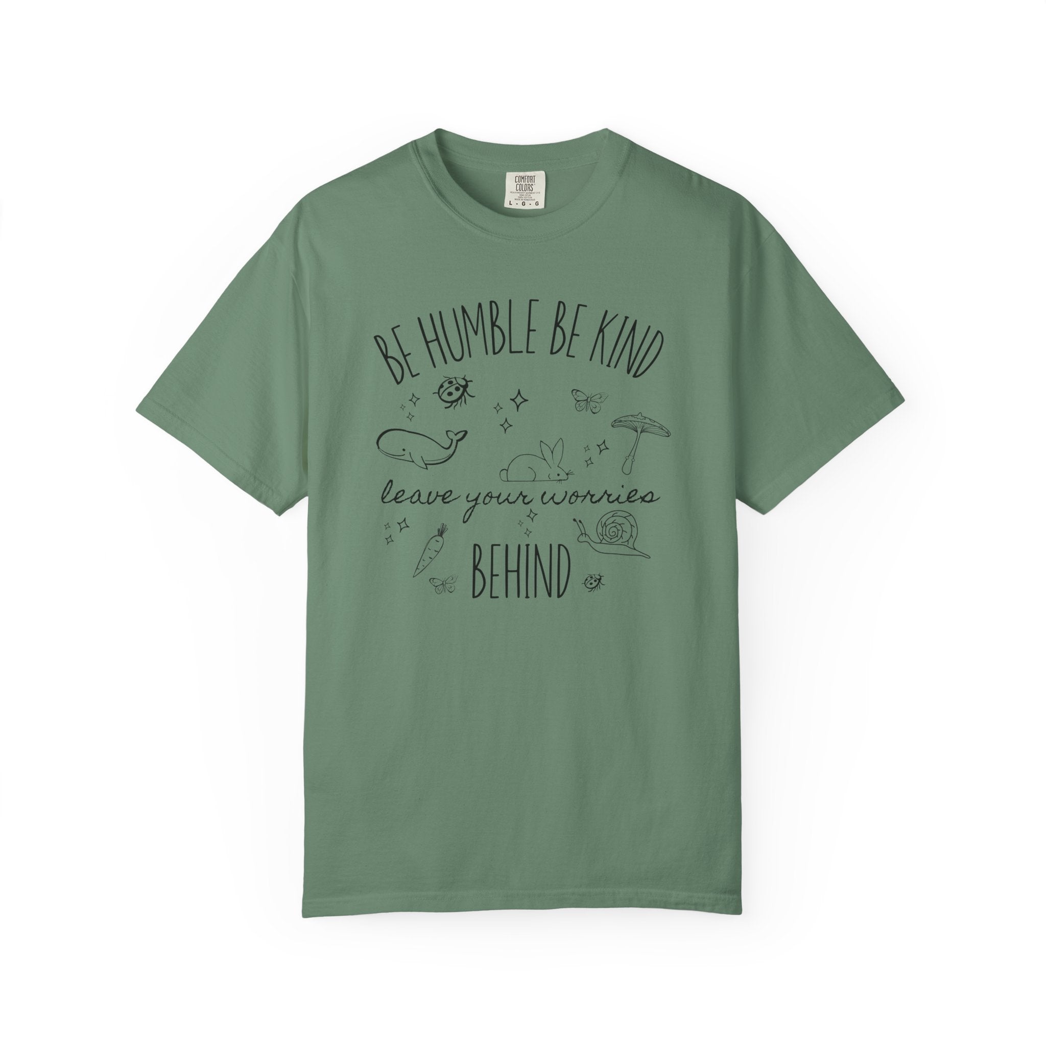 Comfort Colors shirt featuring the quote "Be Humble Be Kind Leave Your Worries Behind" surrounded by whimsical illustrations including a rabbit, whale, mushroom, snail, butterflies, and ladybugs in a cottagecore style.