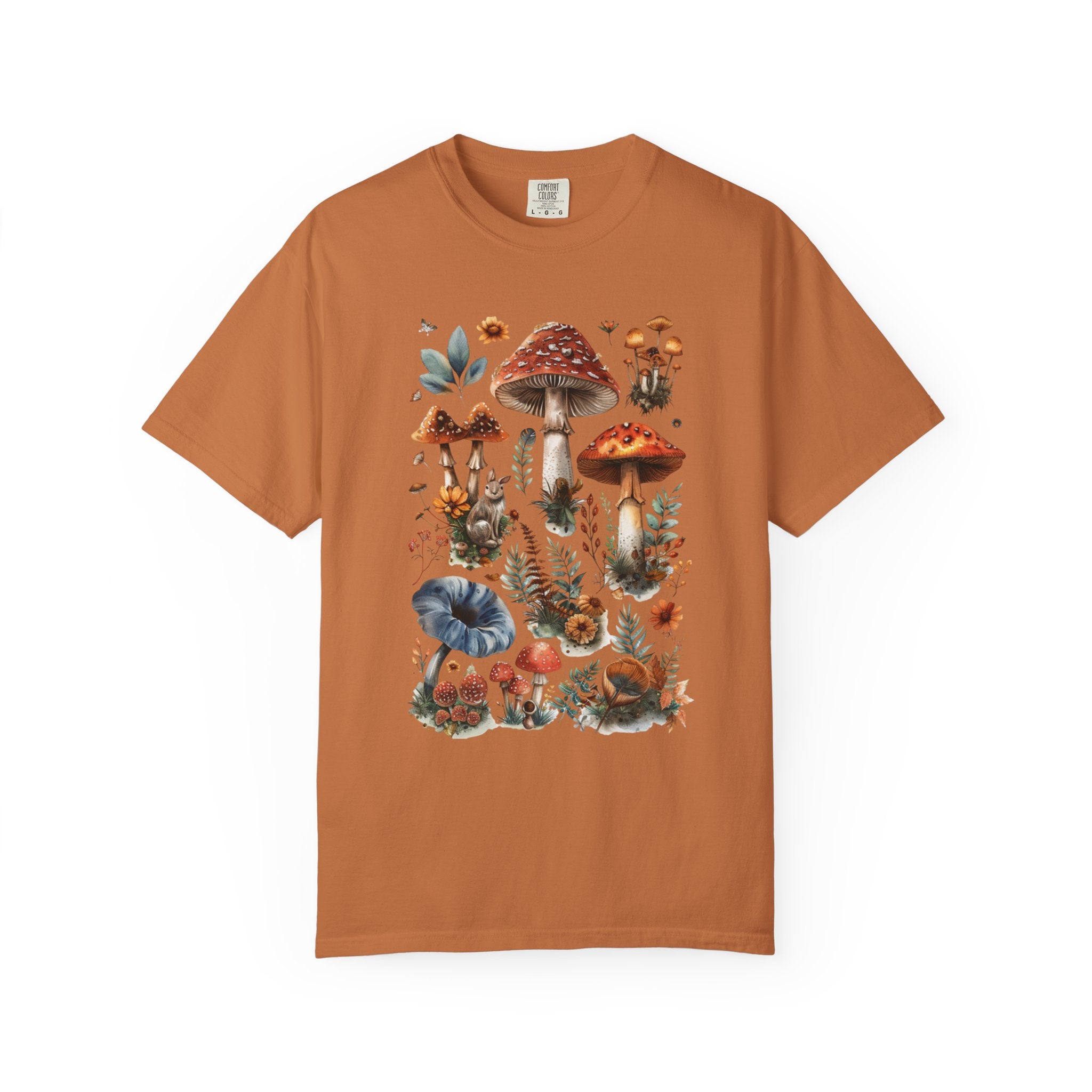 Illustrated woodland collage featuring red and brown mushrooms, leaves, flowers, and forest details in a vintage watercolor style, printed on a Comfort Colors shirt.