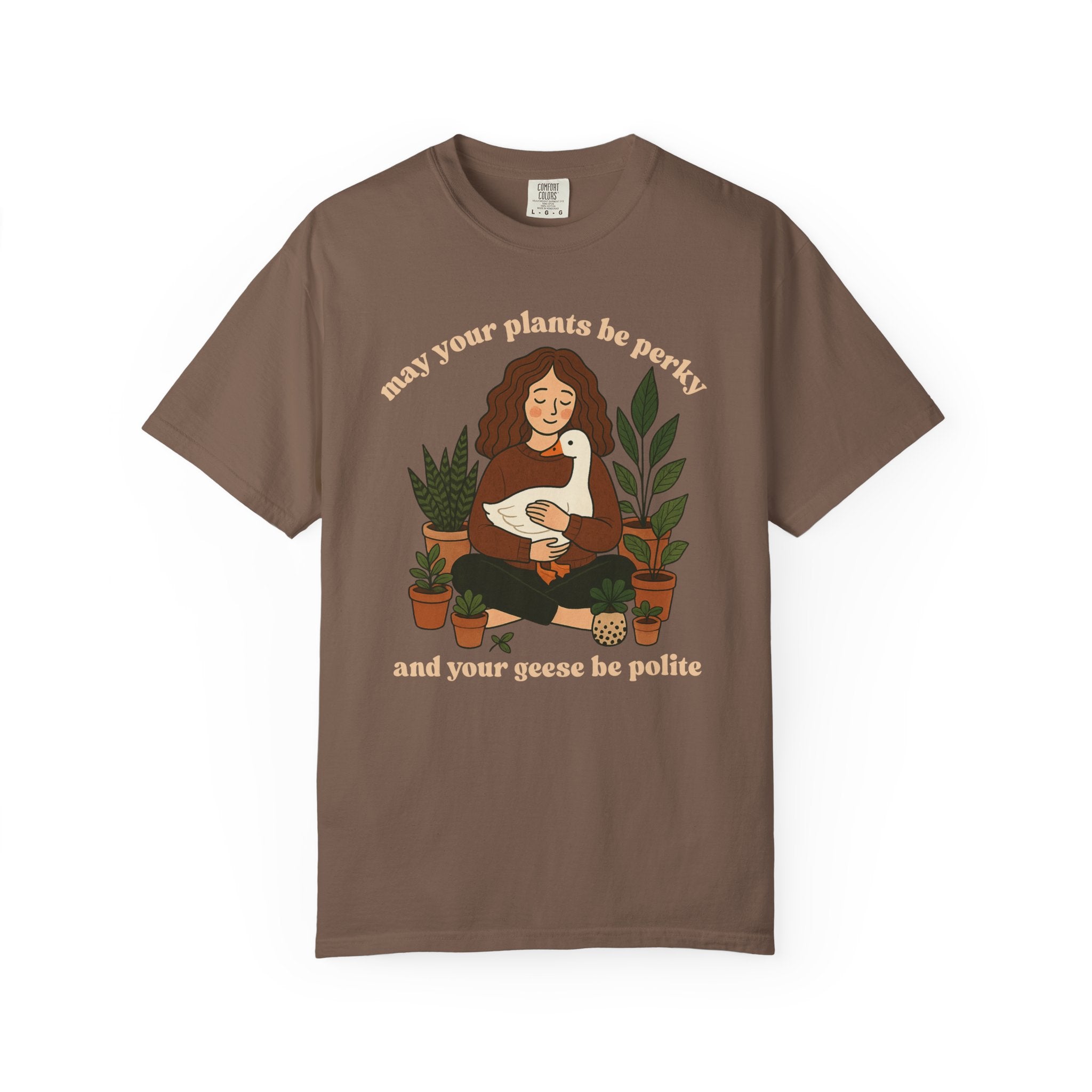 A cozy woman holding a goose surrounded by potted plants with the text “May your plants be perky and your geese be polite” printed on a Comfort Colors cottagecore shirt.