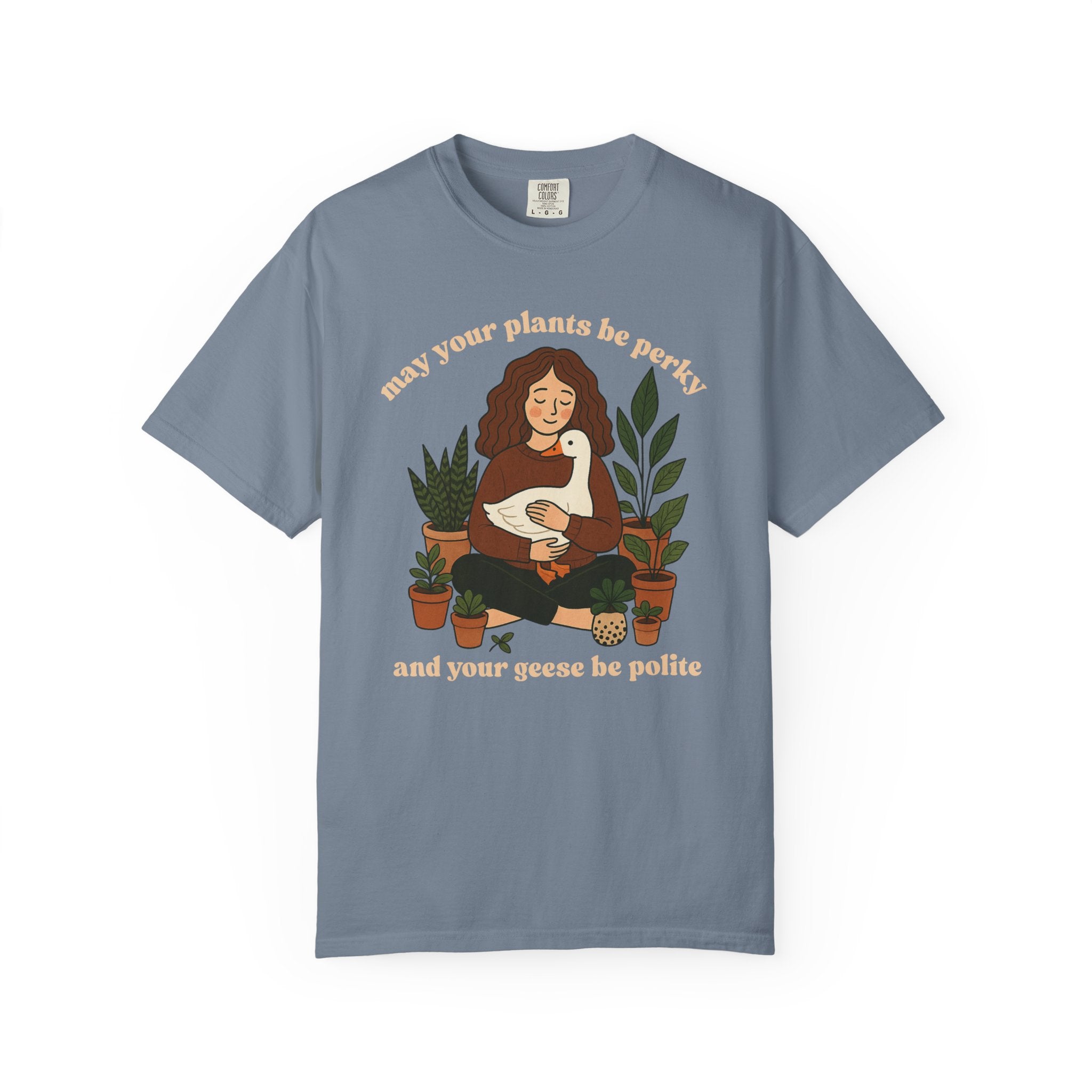A cozy woman holding a goose surrounded by potted plants with the text “May your plants be perky and your geese be polite” printed on a Comfort Colors cottagecore shirt.