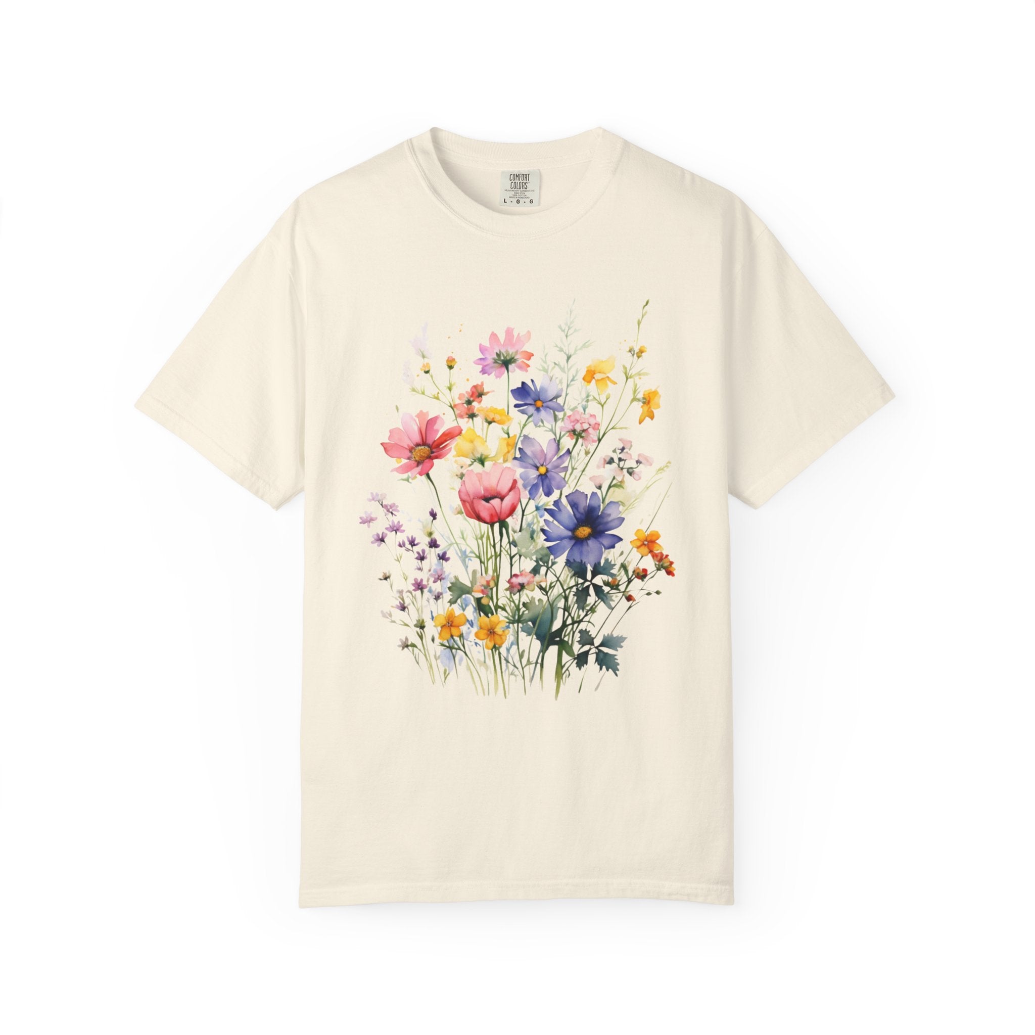 Watercolor-style wildflower meadow illustration with soft pink, yellow, blue, and lavender flowers on green stems, printed on a Comfort Colors shirt.