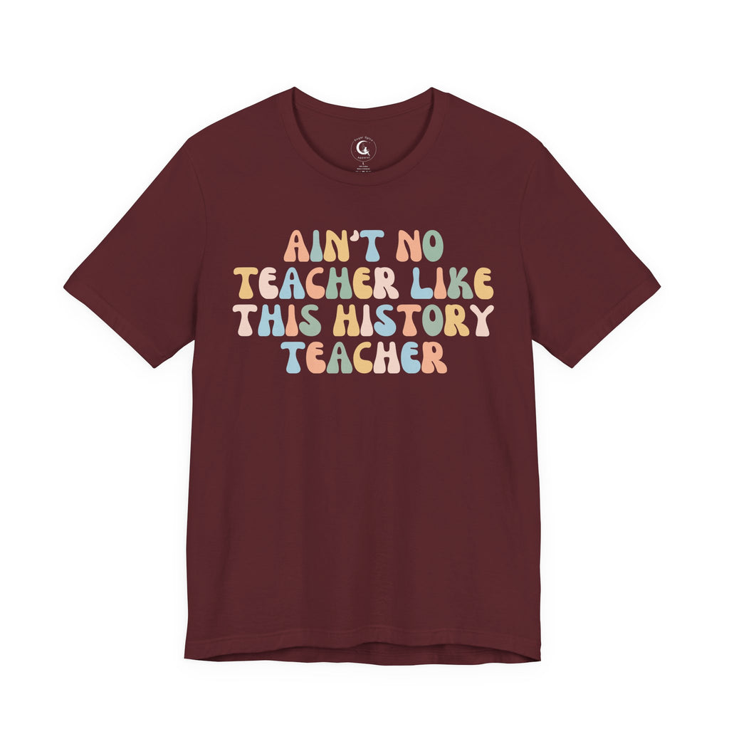 A maroon short-sleeve crewneck t-shirt featuring a retro-style graphic text that reads 'AIN'T NO TEACHER LIKE THIS HISTORY TEACHER' in pastel multicolor letters, displayed on a solid white background.