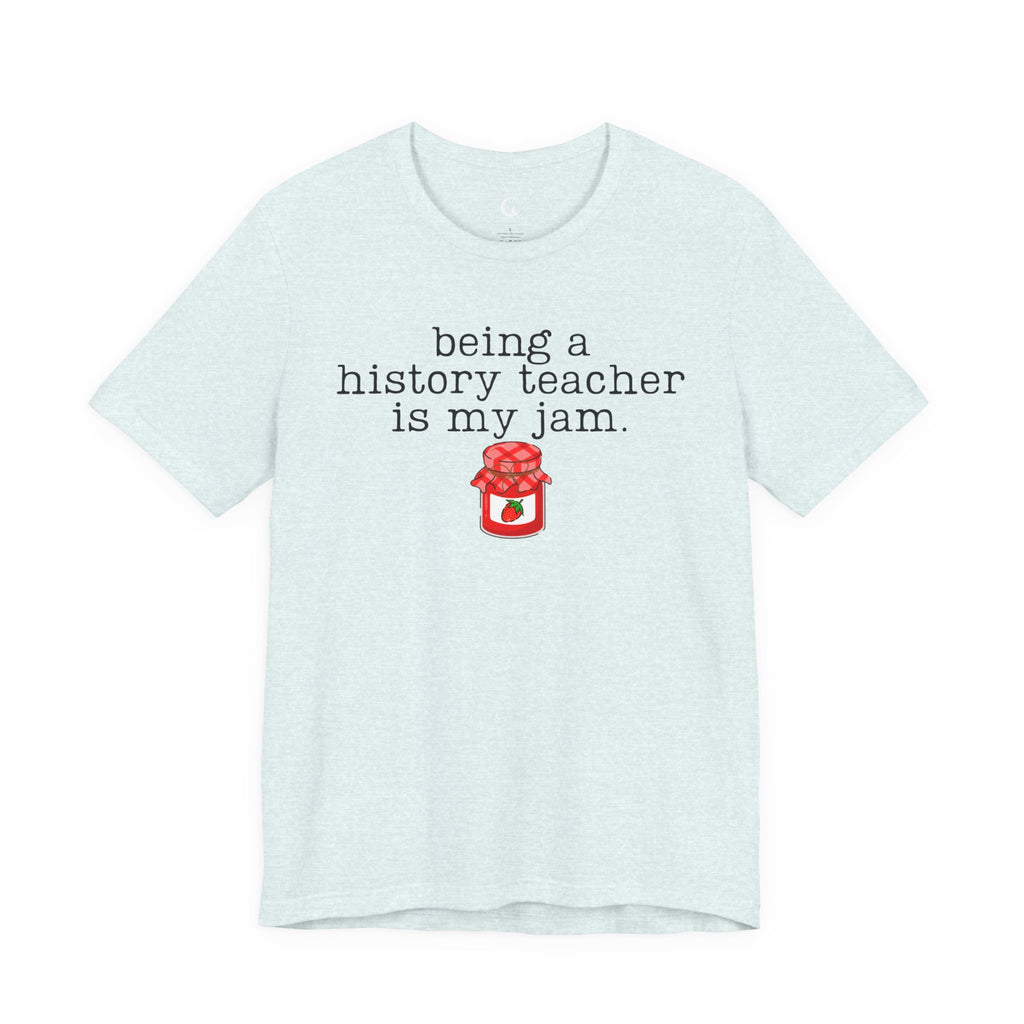 A light heather blue short-sleeve t-shirt with a black typewriter-style text graphic reading 'being a history teacher is my jam.' above a small red jam jar illustration, shown on a plain white background.