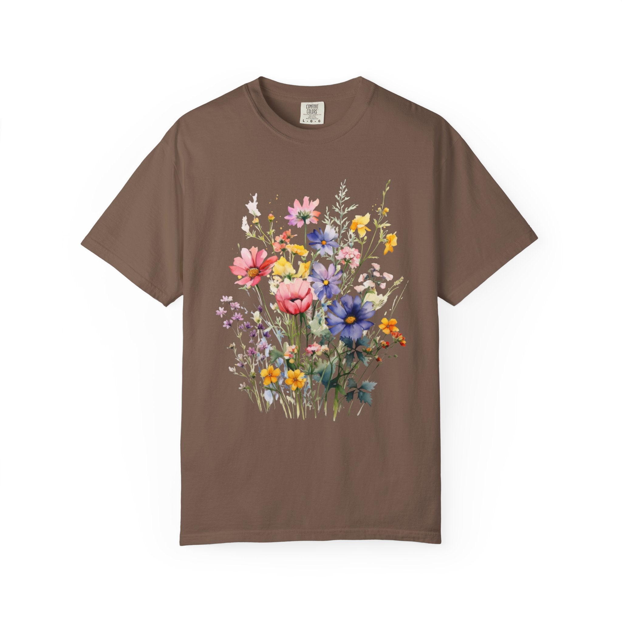 Watercolor-style wildflower meadow illustration with soft pink, yellow, blue, and lavender flowers on green stems, printed on a Comfort Colors shirt.