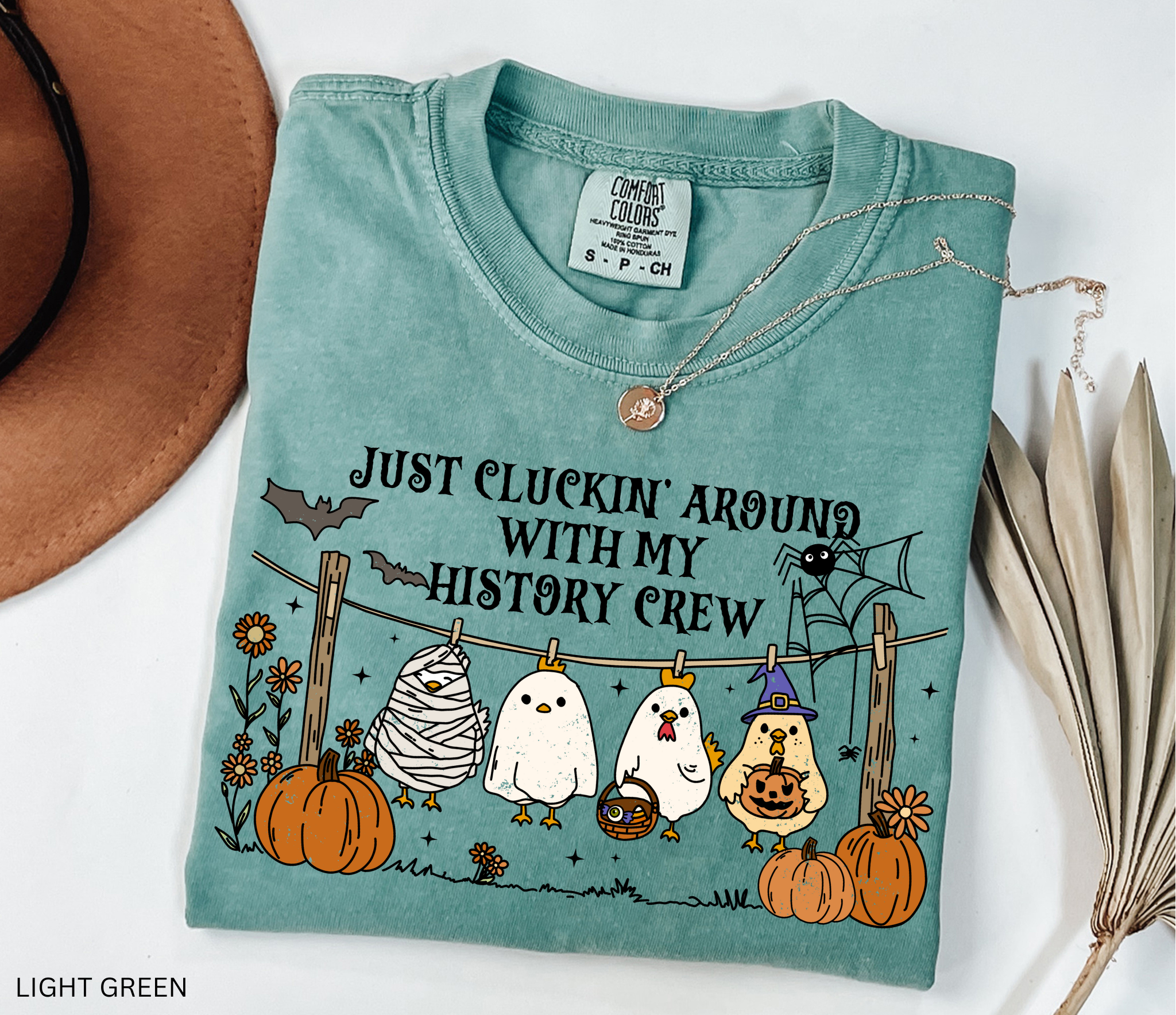 Halloween history teacher shirt with four cartoon chickens dressed in costumes (mummy, ghost, witch, and trick-or-treater) standing on a clothesline with pumpkins and bats, designed as a funny teacher Halloween graphic tee.