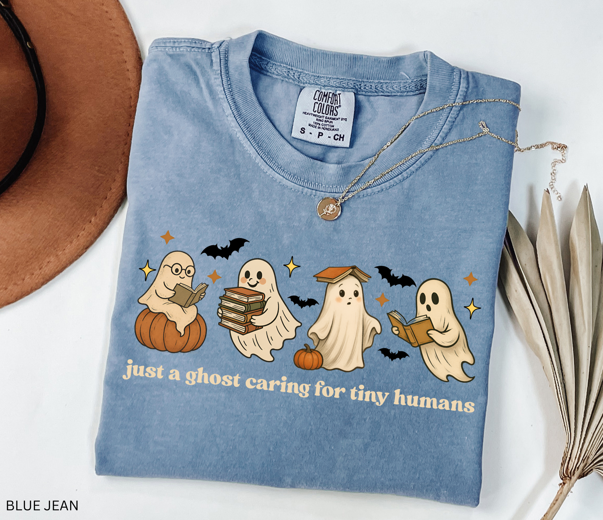 Daycare teacher Halloween shirt with cute ghost characters reading books, sitting on pumpkins, and the phrase ‘Just a ghost caring for tiny humans.