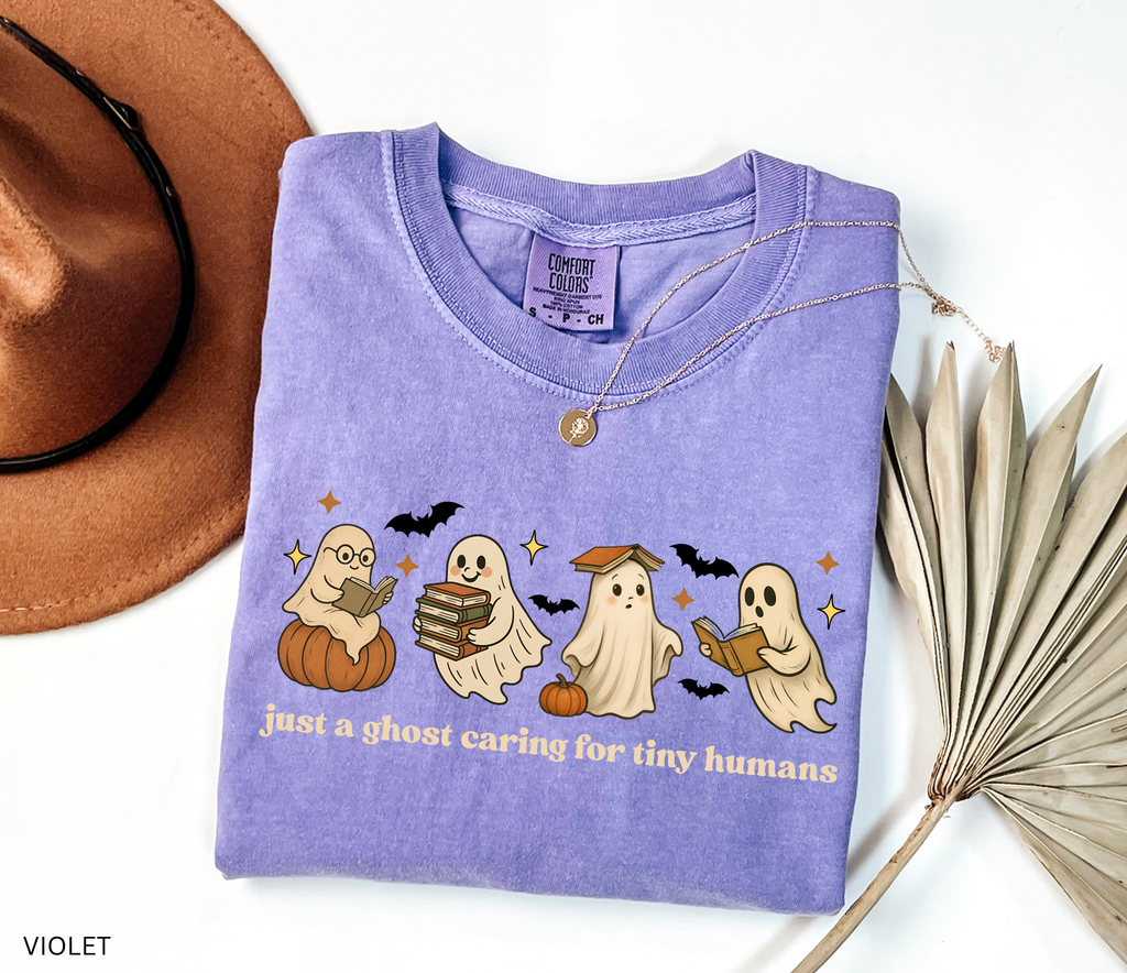 Daycare teacher Halloween shirt with cute ghost characters reading books, sitting on pumpkins, and the phrase ‘Just a ghost caring for tiny humans.