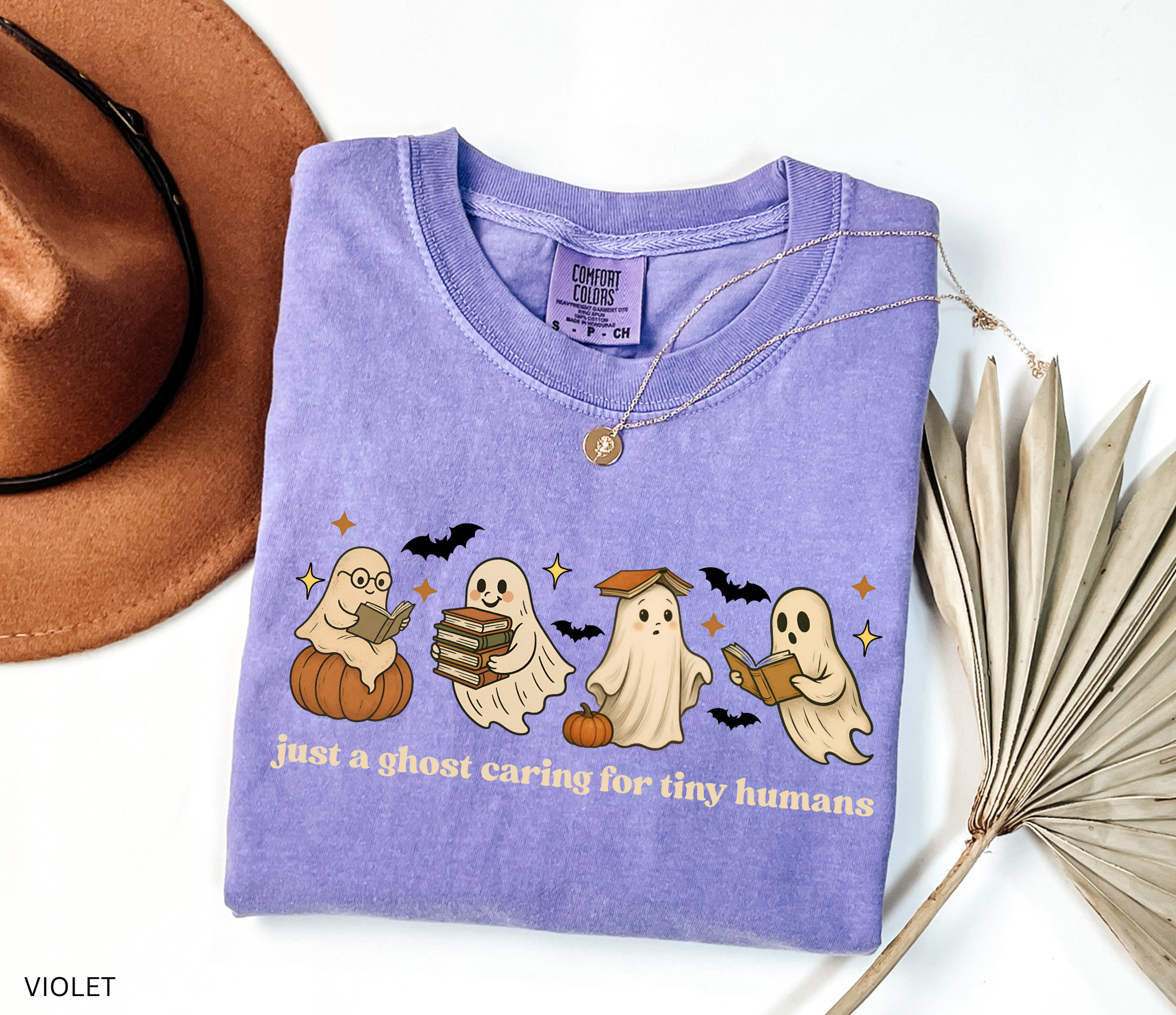 Daycare teacher Halloween shirt with cute ghost characters reading books, sitting on pumpkins, and the phrase ‘Just a ghost caring for tiny humans.