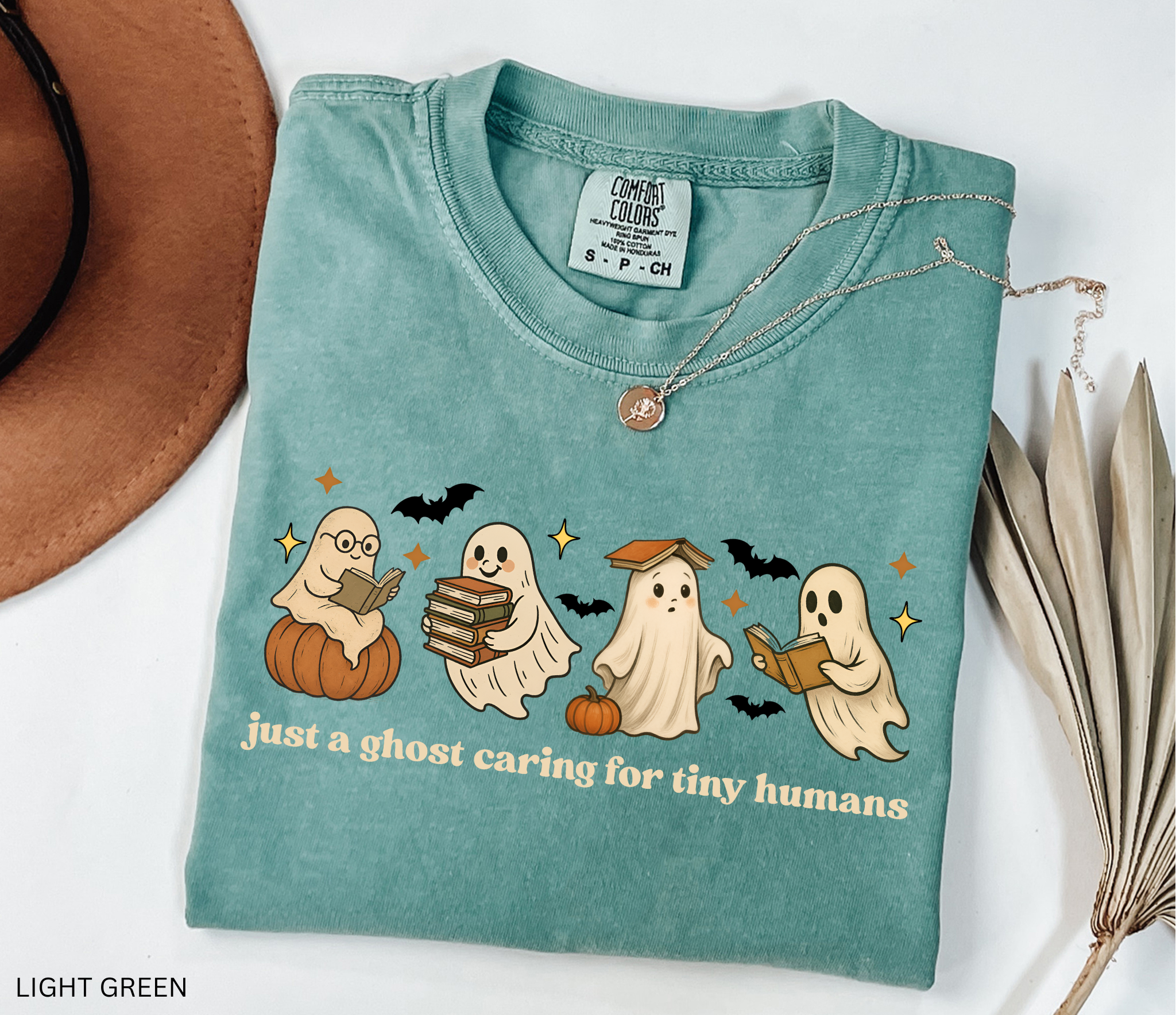 Daycare teacher Halloween shirt with cute ghost characters reading books, sitting on pumpkins, and the phrase ‘Just a ghost caring for tiny humans.