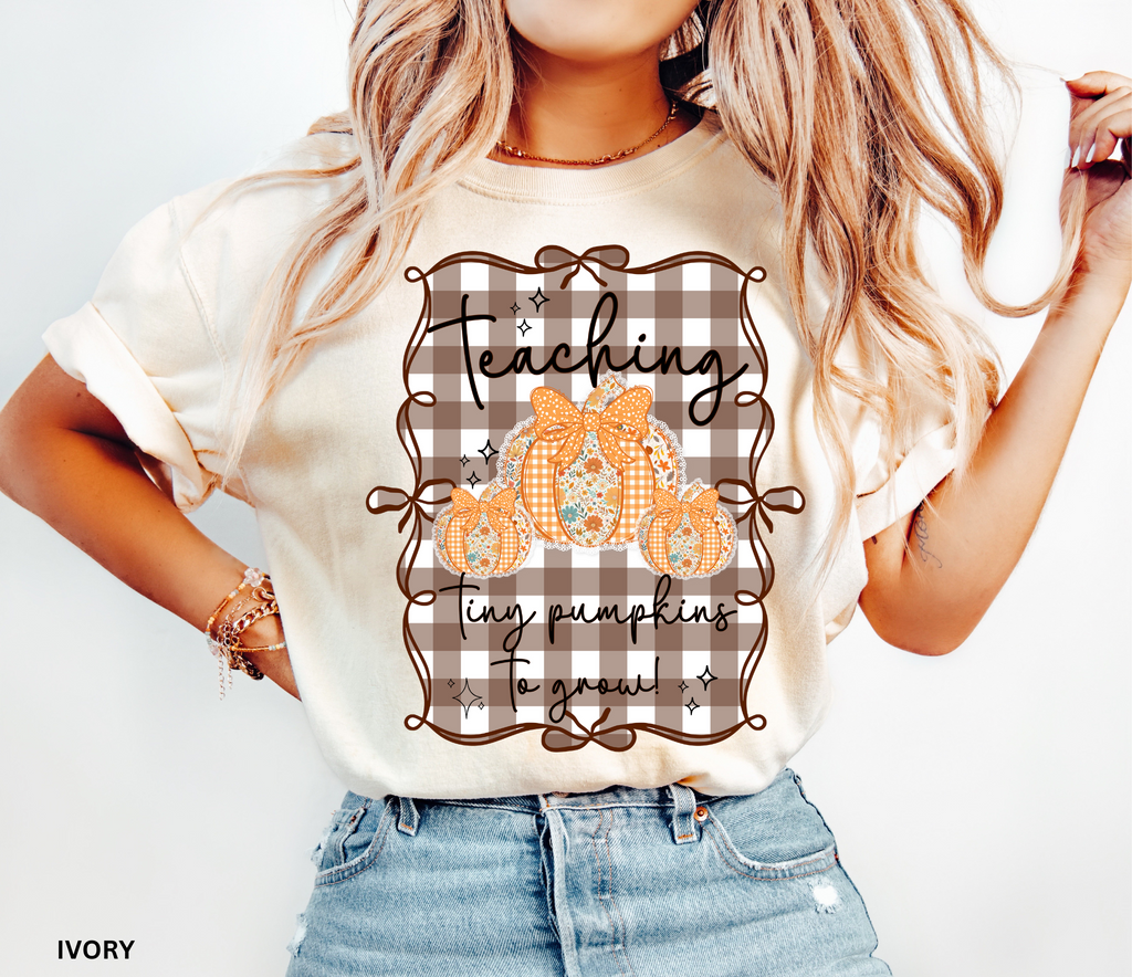 Brown gingham background Halloween teacher shirt with three floral orange pumpkins tied in bows and the phrase “Teaching Tiny Pumpkins to Grow.”