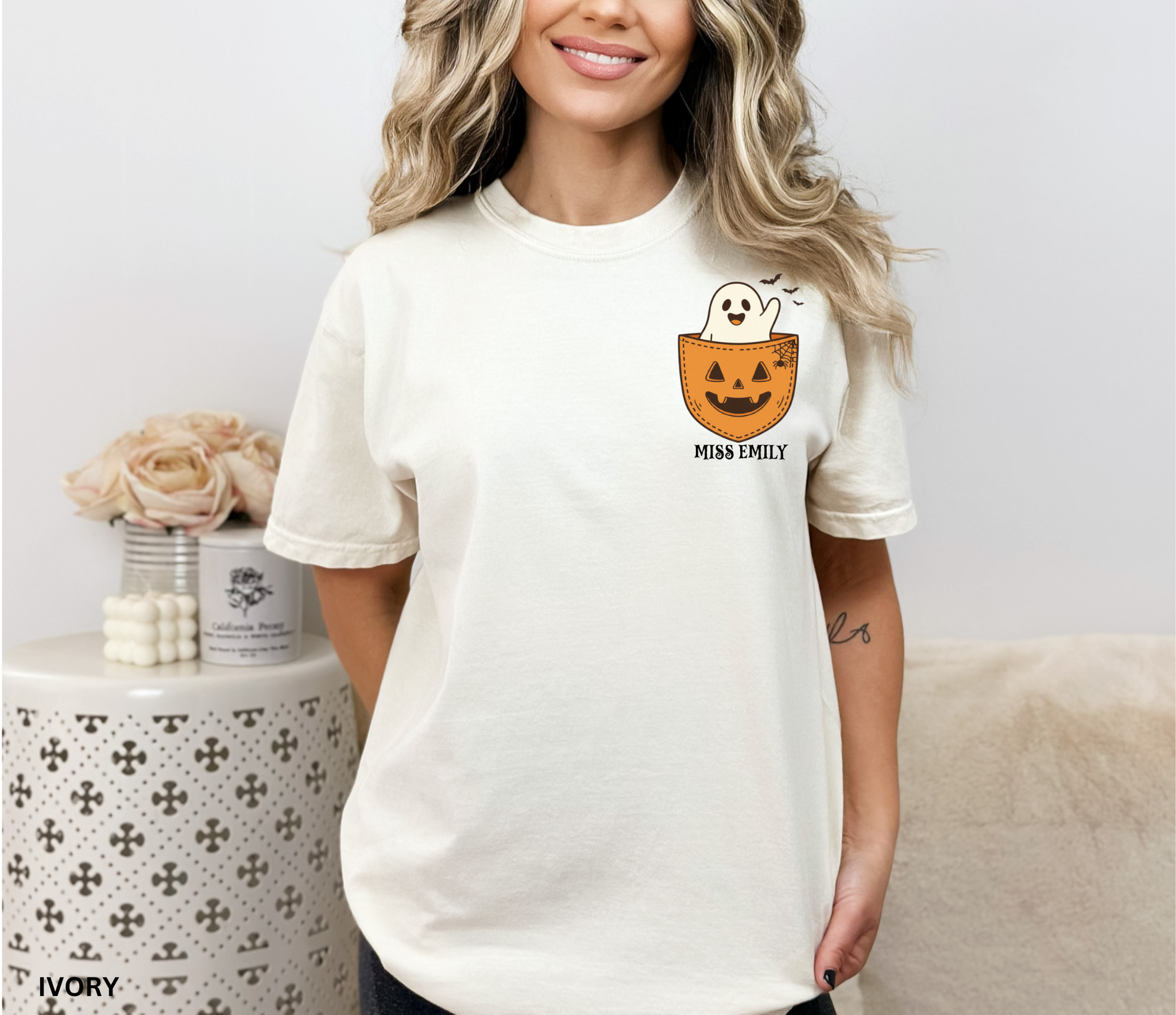 Halloween teacher shirt with a smiling ghost peeking out of a jack-o’-lantern pocket, bats, and spiderweb detail.