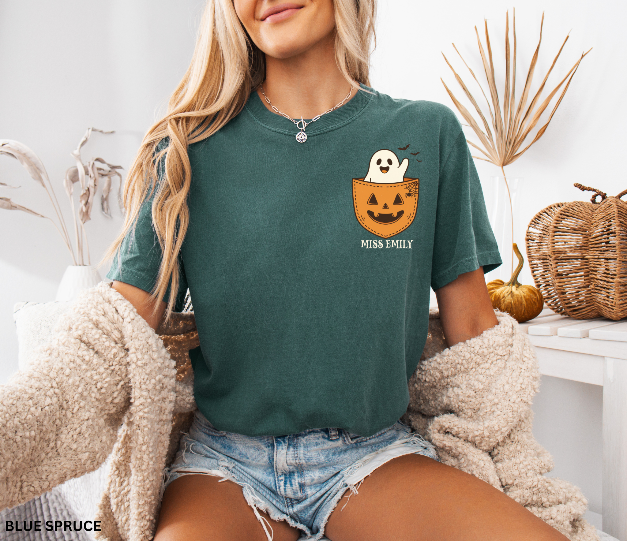 Halloween teacher shirt with a smiling ghost peeking out of a jack-o’-lantern pocket, bats, and spiderweb detail.