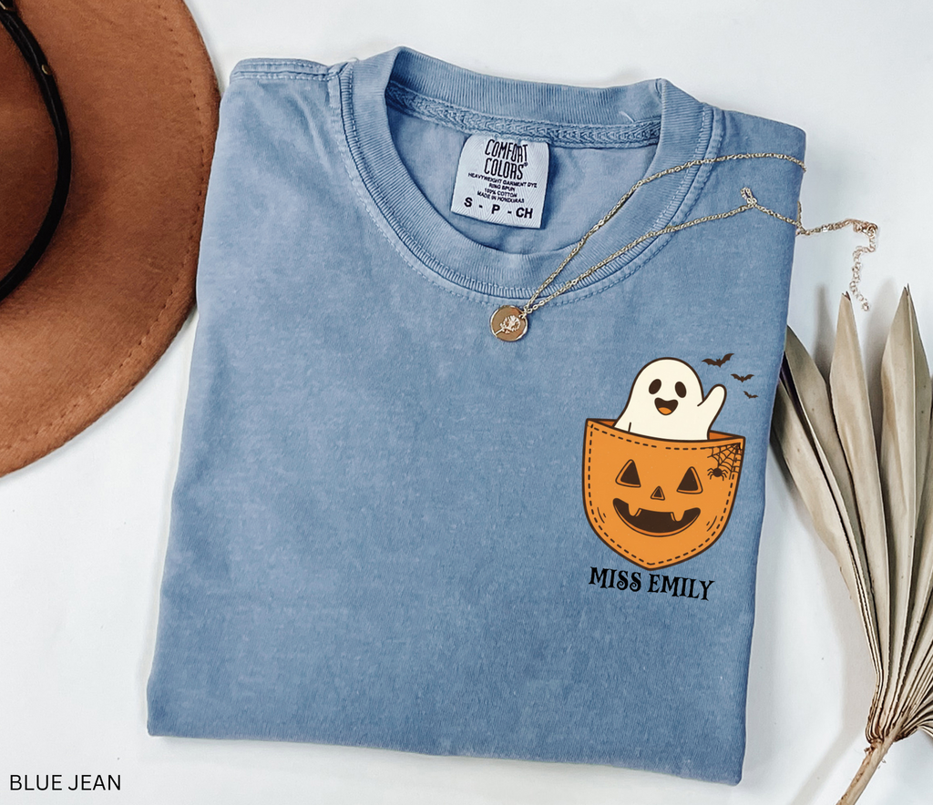 Halloween teacher shirt with a smiling ghost peeking out of a jack-o’-lantern pocket, bats, and spiderweb detail.