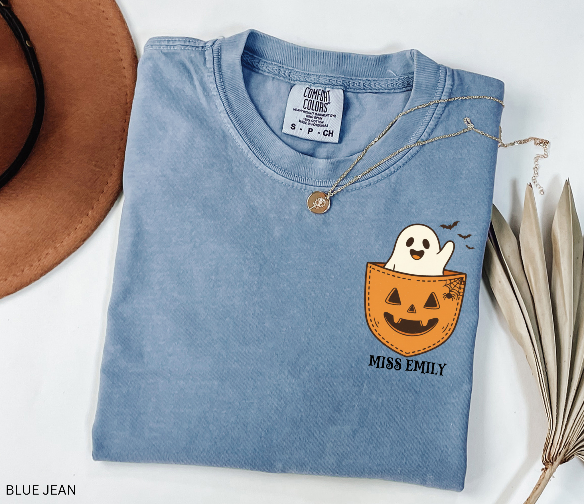 Halloween teacher shirt with a smiling ghost peeking out of a jack-o’-lantern pocket, bats, and spiderweb detail.