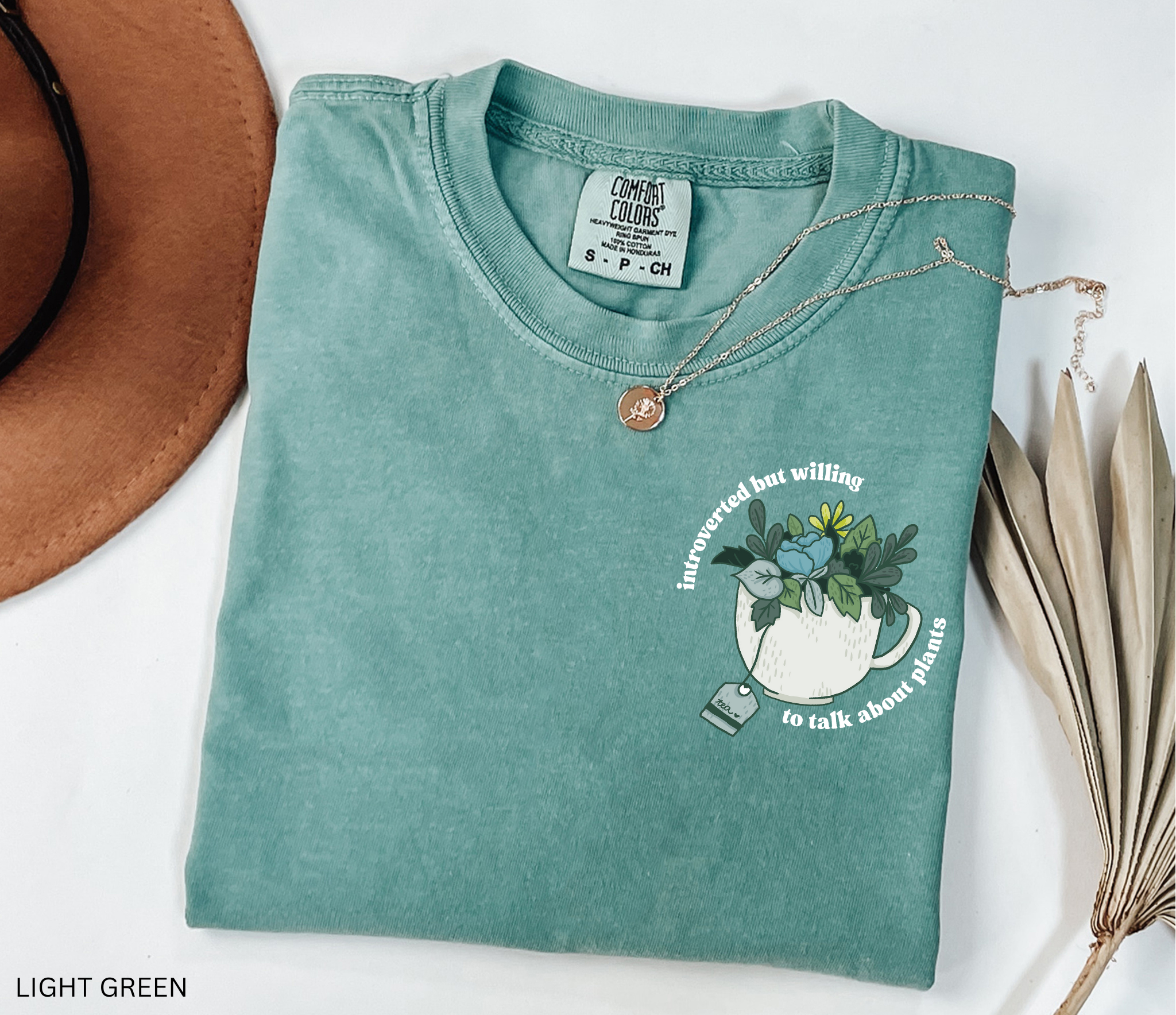 Illustrated cottagecore teacup filled with leafy green plants and flowers, with the phrase “introverted but willing to talk about plants” in curved lettering.