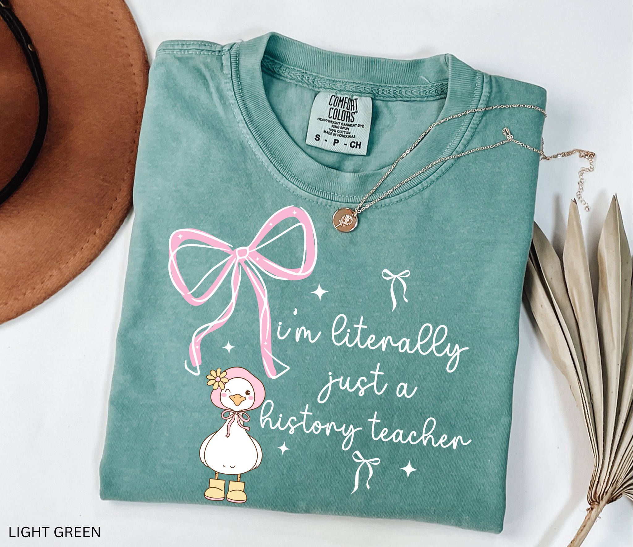 Funny history teacher shirt with a cute goose, pink bows, and the phrase ‘I’m literally just a history teacher.’ Coquette aesthetic social studies tee.