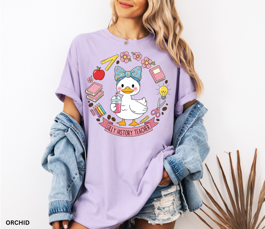 Funny history teacher shirt with a goose wearing a bow, surrounded by school doodles like books, pencils, apple, and scissors. Reads ‘Silly History Teacher.