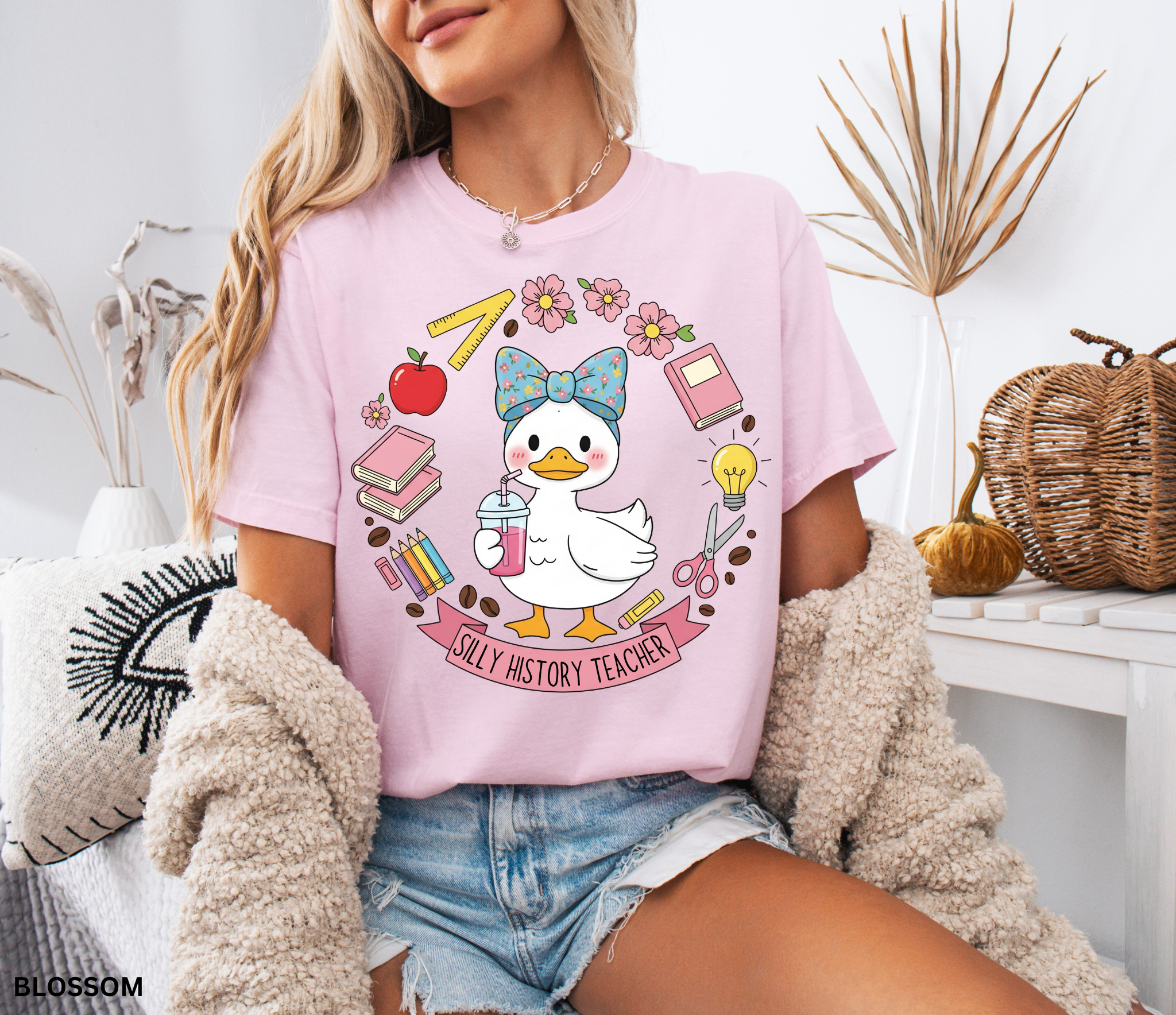 Funny history teacher shirt with a goose wearing a bow, surrounded by school doodles like books, pencils, apple, and scissors. Reads ‘Silly History Teacher.