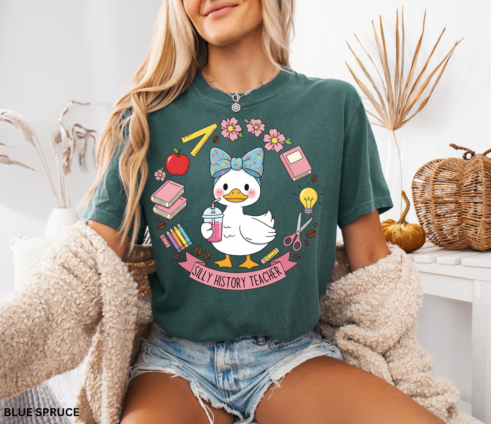 Funny history teacher shirt with a goose wearing a bow, surrounded by school doodles like books, pencils, apple, and scissors. Reads ‘Silly History Teacher.