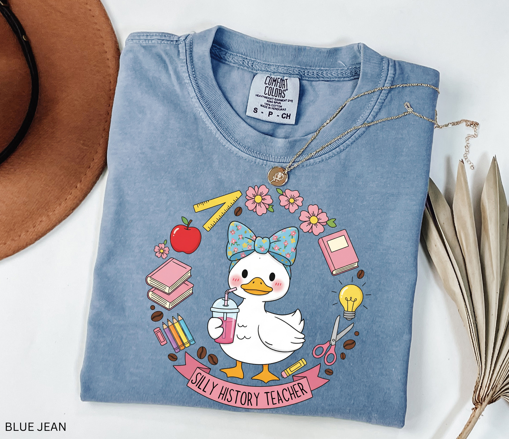 Funny history teacher shirt with a goose wearing a bow, surrounded by school doodles like books, pencils, apple, and scissors. Reads ‘Silly History Teacher.