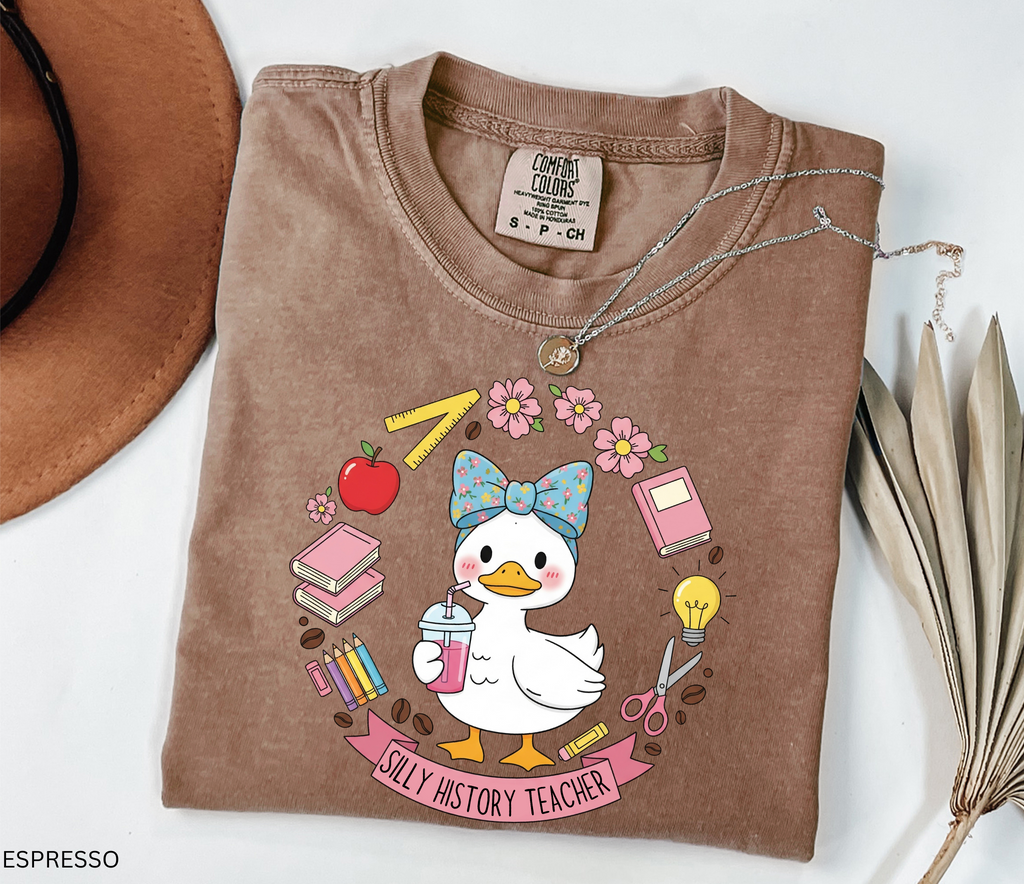 Funny history teacher shirt with a goose wearing a bow, surrounded by school doodles like books, pencils, apple, and scissors. Reads ‘Silly History Teacher.