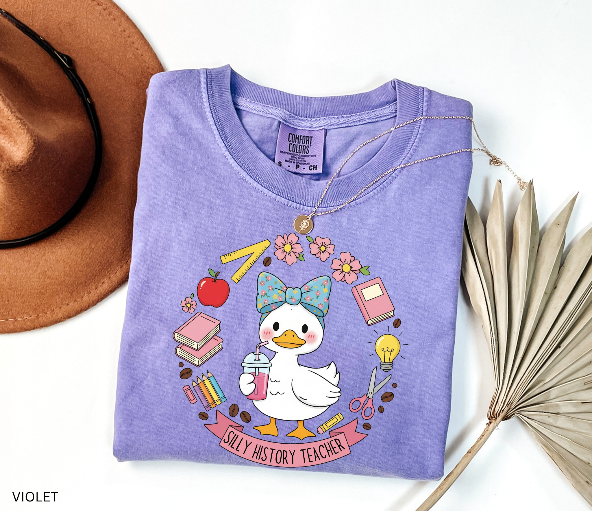 Funny history teacher shirt with a goose wearing a bow, surrounded by school doodles like books, pencils, apple, and scissors. Reads ‘Silly History Teacher.