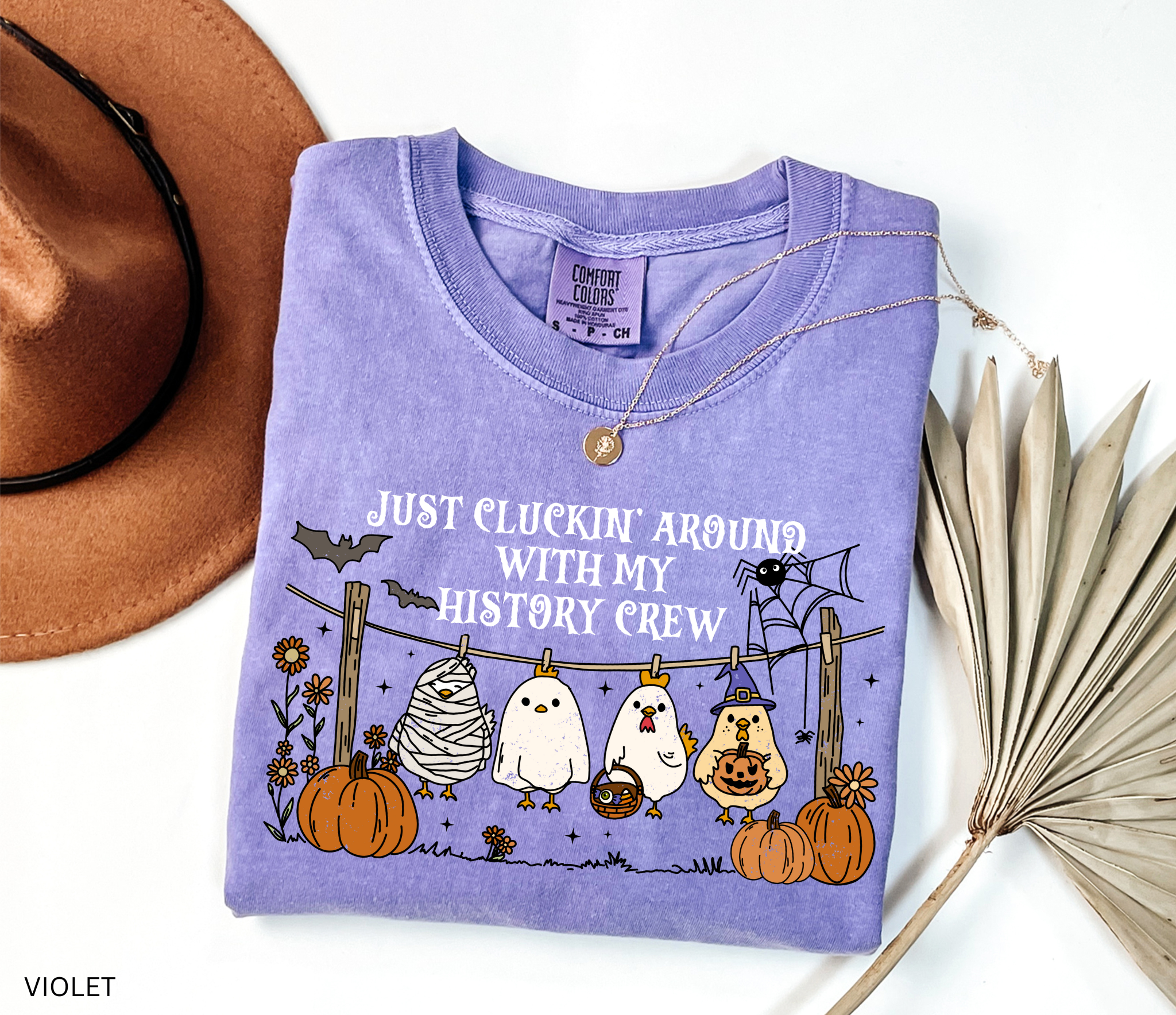 Halloween history teacher shirt with chickens in costumes on a clothesline, pumpkins, bats, and the phrase ‘Just cluckin’ around with my history crew.’ Funny group teacher shirt.