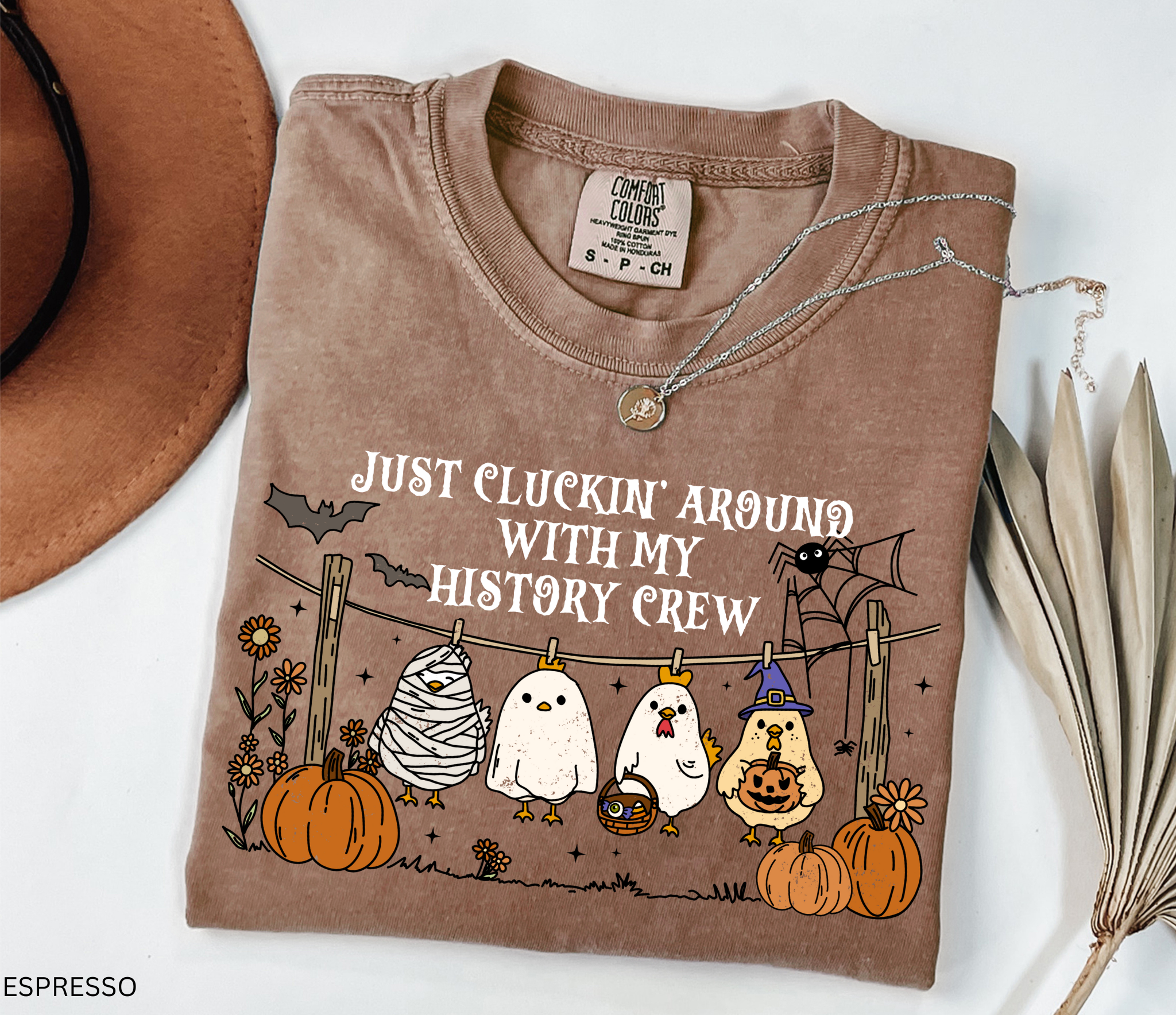 Halloween history teacher shirt with chickens in costumes on a clothesline, pumpkins, bats, and the phrase ‘Just cluckin’ around with my history crew.’ Funny group teacher shirt.