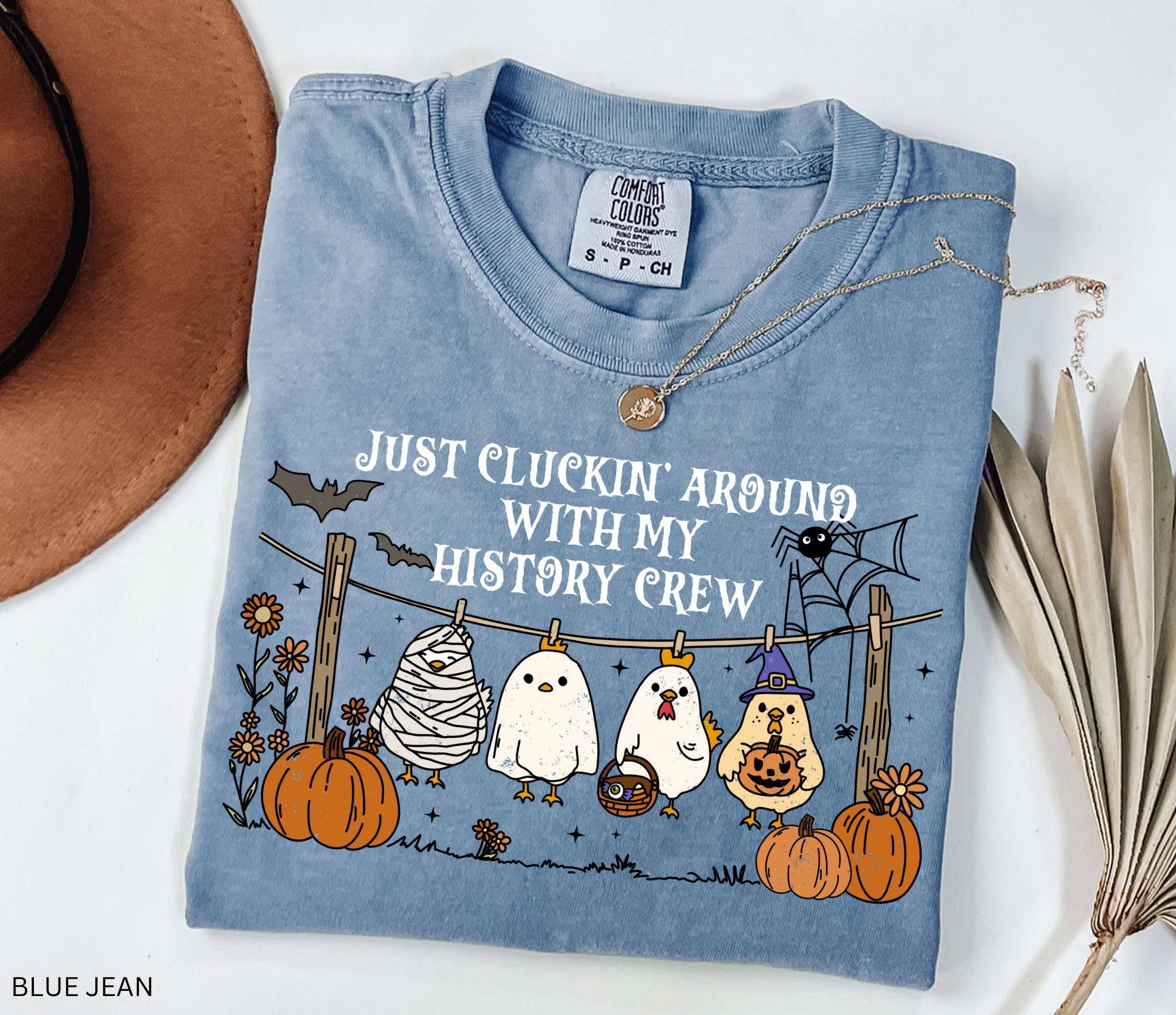 Halloween history teacher shirt with chickens in costumes on a clothesline, pumpkins, bats, and the phrase ‘Just cluckin’ around with my history crew.’ Funny group teacher shirt.