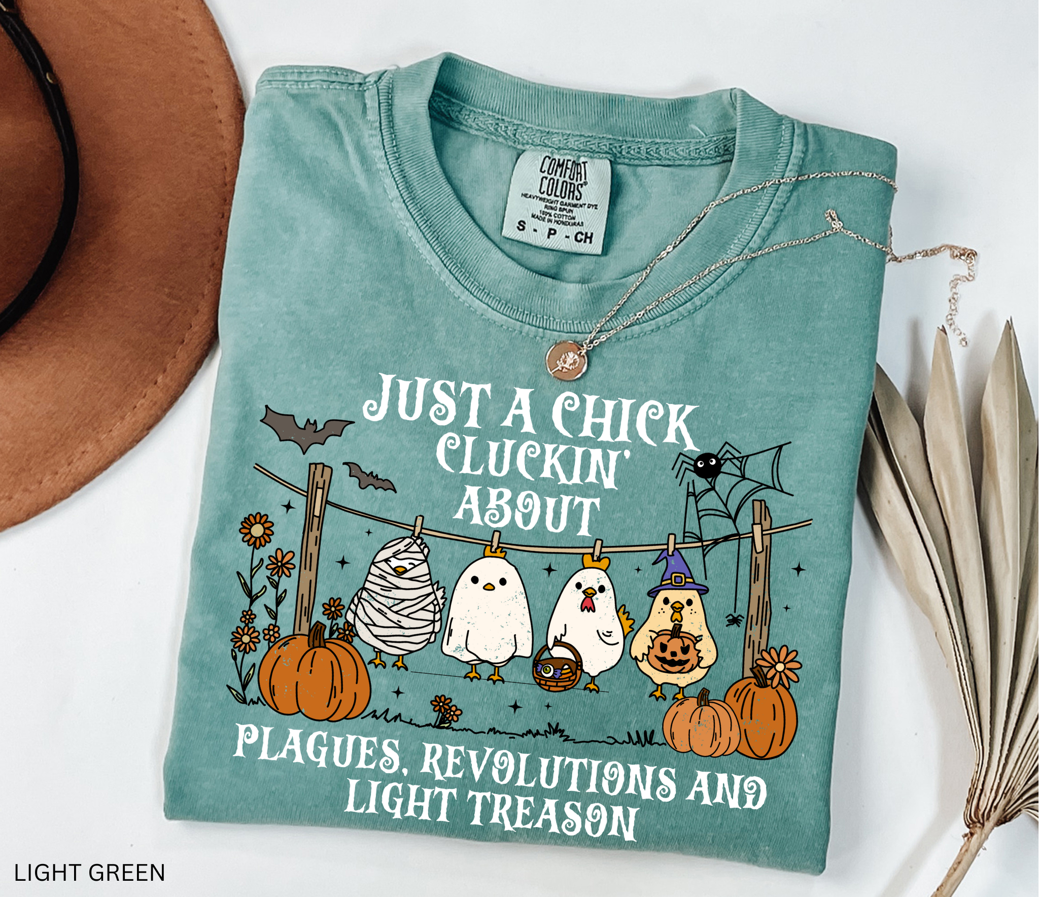 Halloween history teacher shirt with chickens in costumes, pumpkins, and text that reads ‘Just a chick cluckin’ about plagues, revolutions, and light treason.’ Funny spooky teacher tee