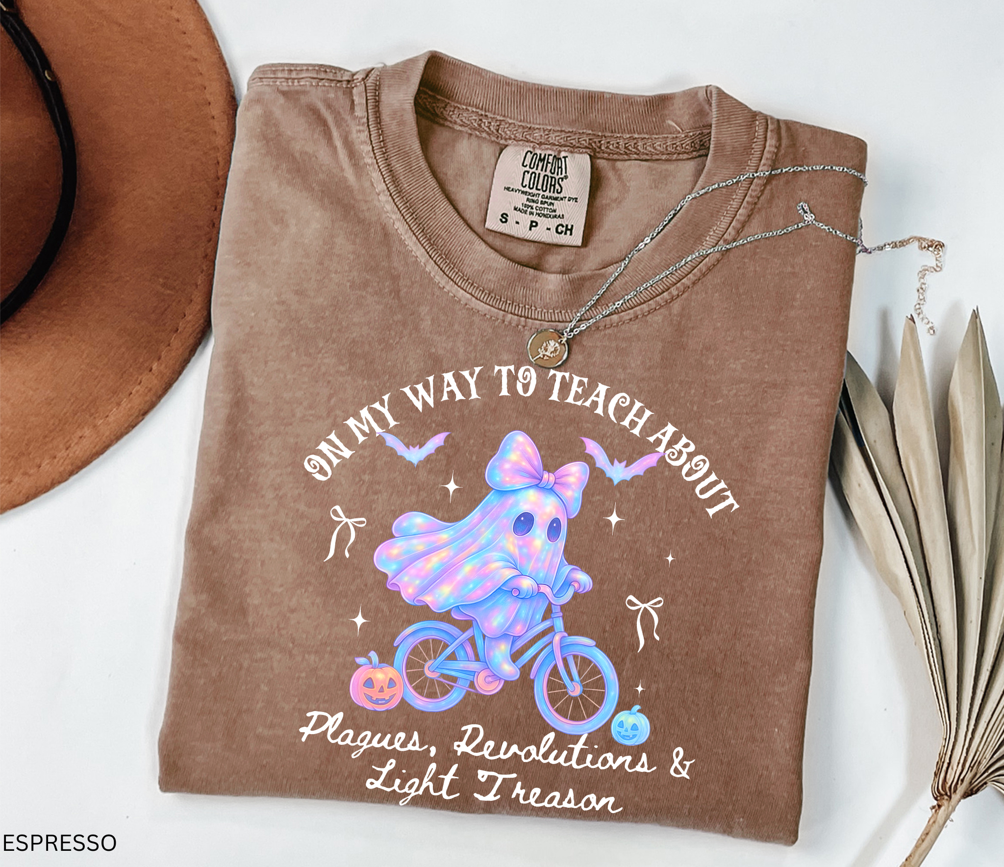 Halloween teacher shirt design with a glowing pastel ghost wearing a bow, riding a bicycle surrounded by pumpkins, bats, and stars. A whimsical spooky-season graphic perfect for history teachers.