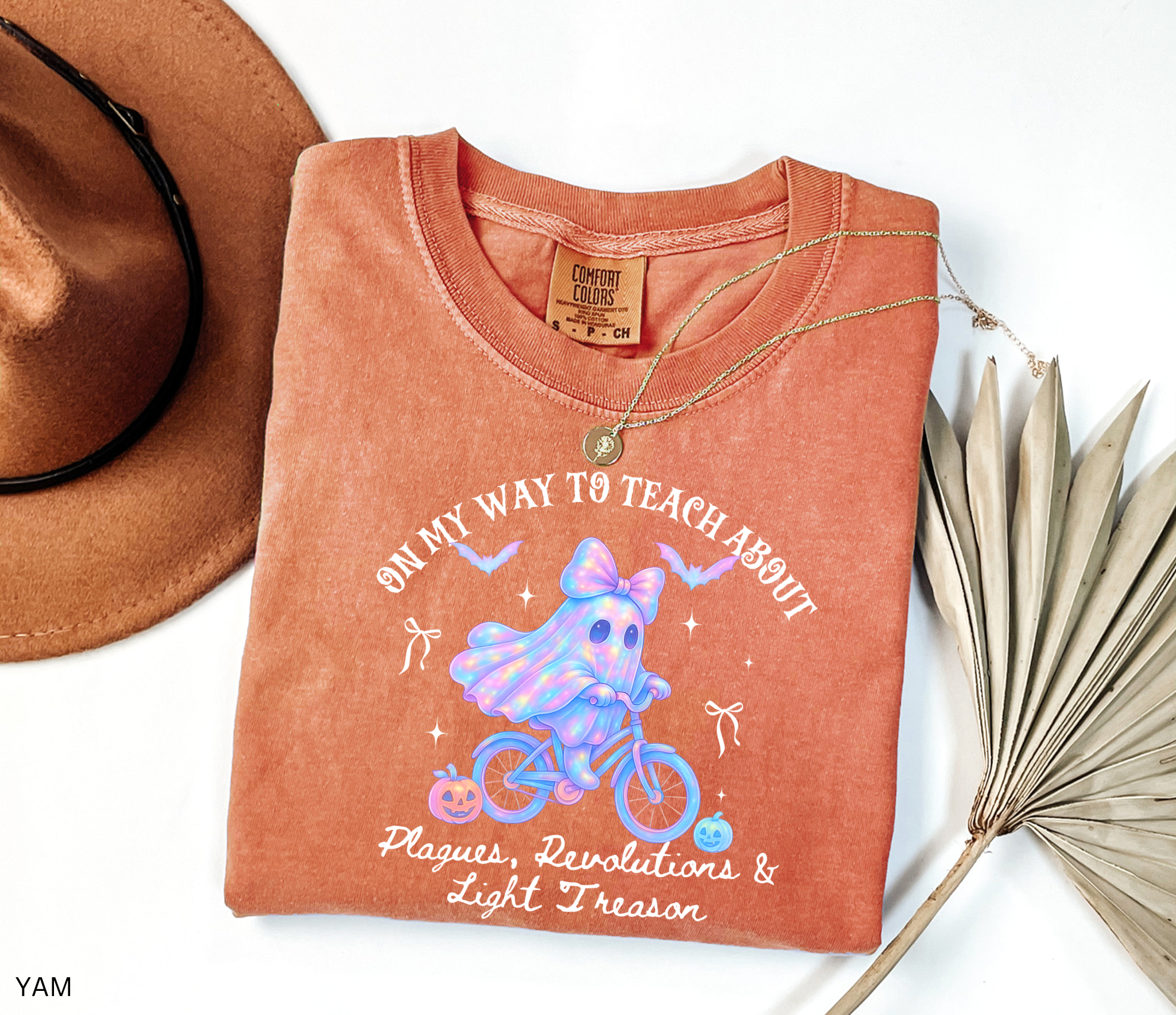 Halloween teacher shirt design with a glowing pastel ghost wearing a bow, riding a bicycle surrounded by pumpkins, bats, and stars. A whimsical spooky-season graphic perfect for history teachers.