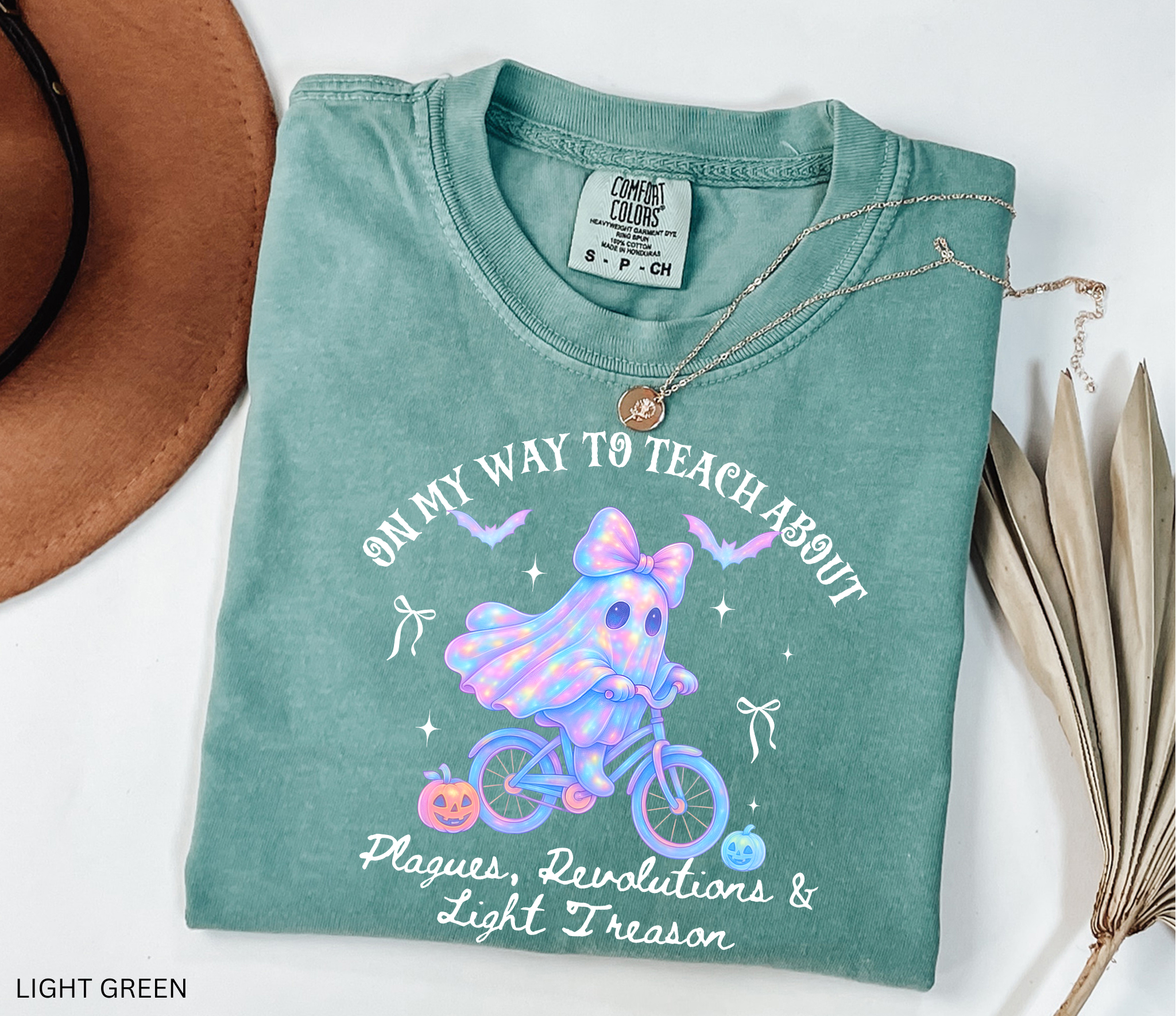Halloween teacher shirt design with a glowing pastel ghost wearing a bow, riding a bicycle surrounded by pumpkins, bats, and stars. A whimsical spooky-season graphic perfect for history teachers.
