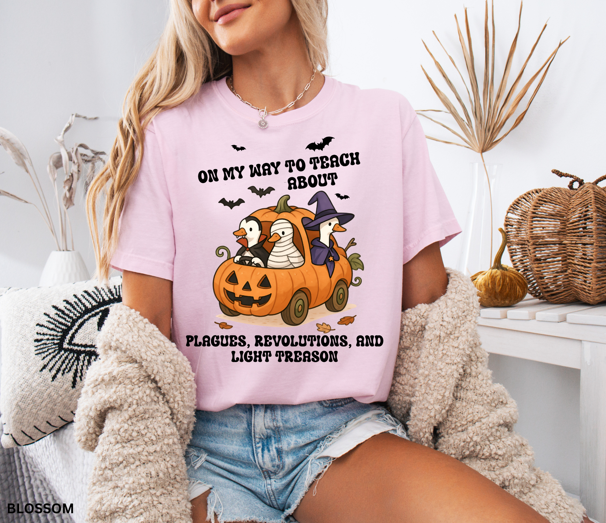 Halloween shirt design with geese dressed as Dracula, a mummy, and a witch riding in a carved pumpkin car, with bats and autumn leaves around. A playful and spooky history teacher graphic.