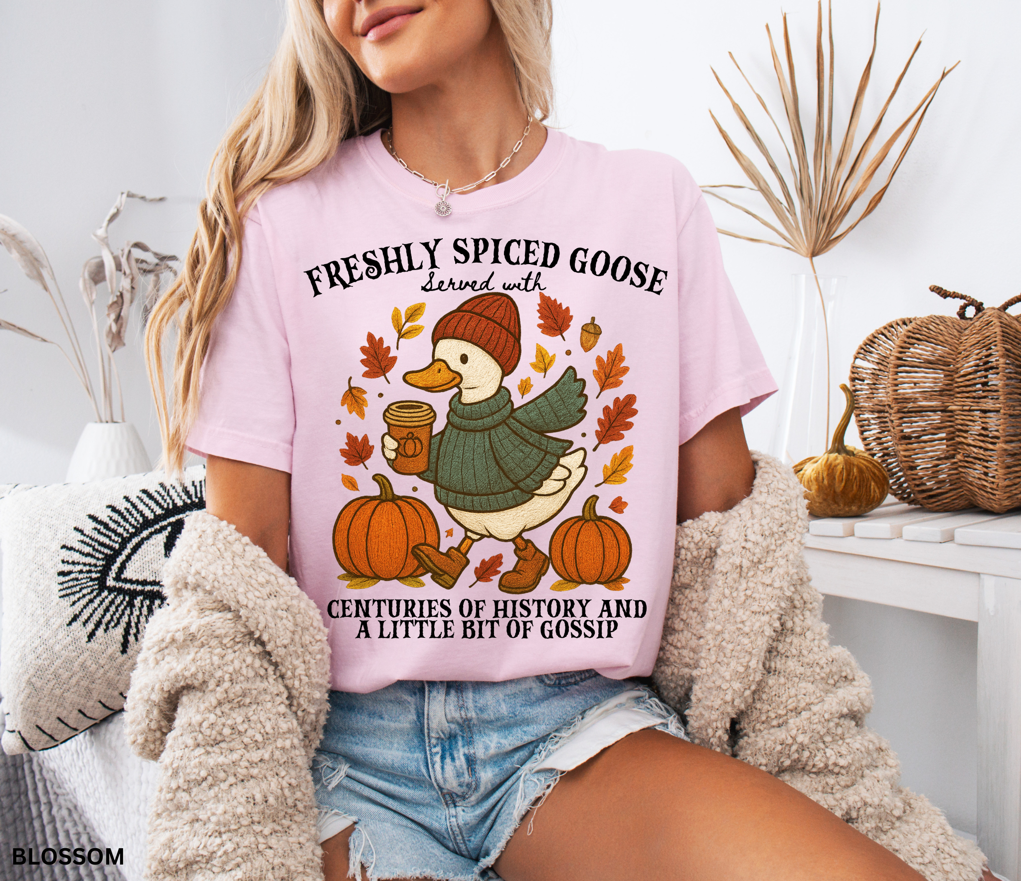 Cozy fall shirt design featuring a goose in a sweater and beanie holding pumpkin spice coffee, surrounded by pumpkins and autumn leaves – made for history teachers and professors.