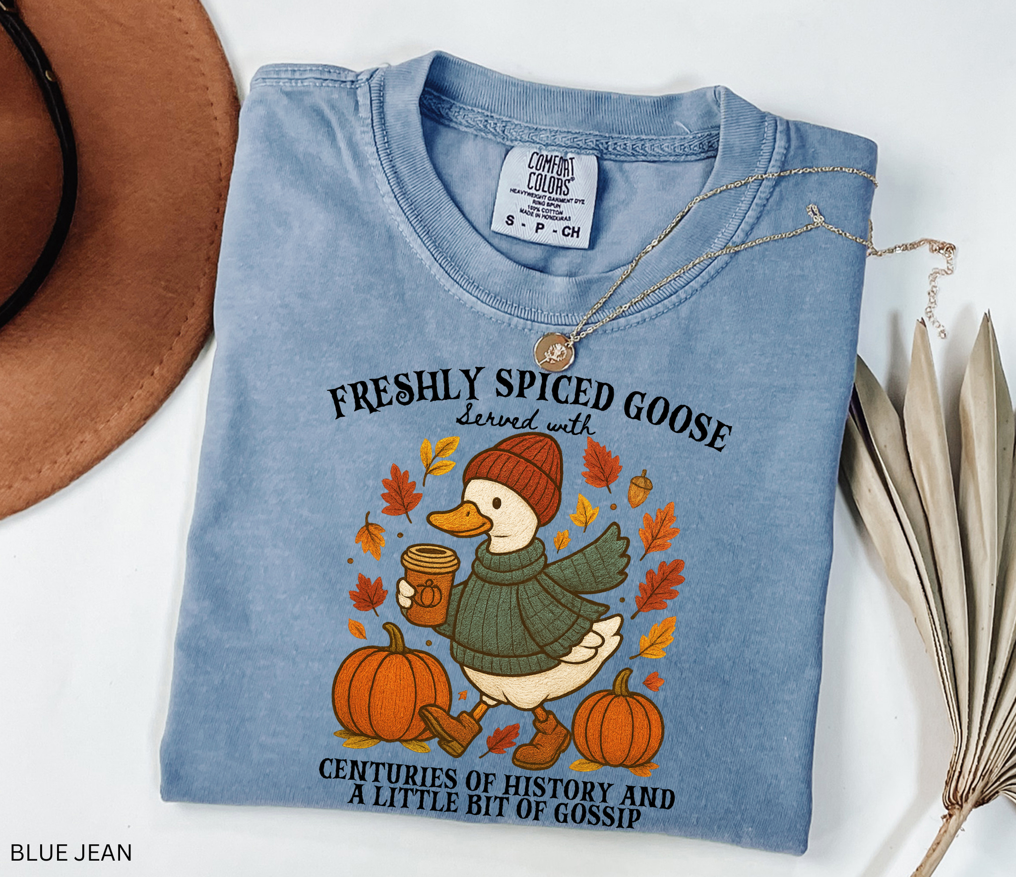 Cozy fall shirt design featuring a goose in a sweater and beanie holding pumpkin spice coffee, surrounded by pumpkins and autumn leaves – made for history teachers and professors.