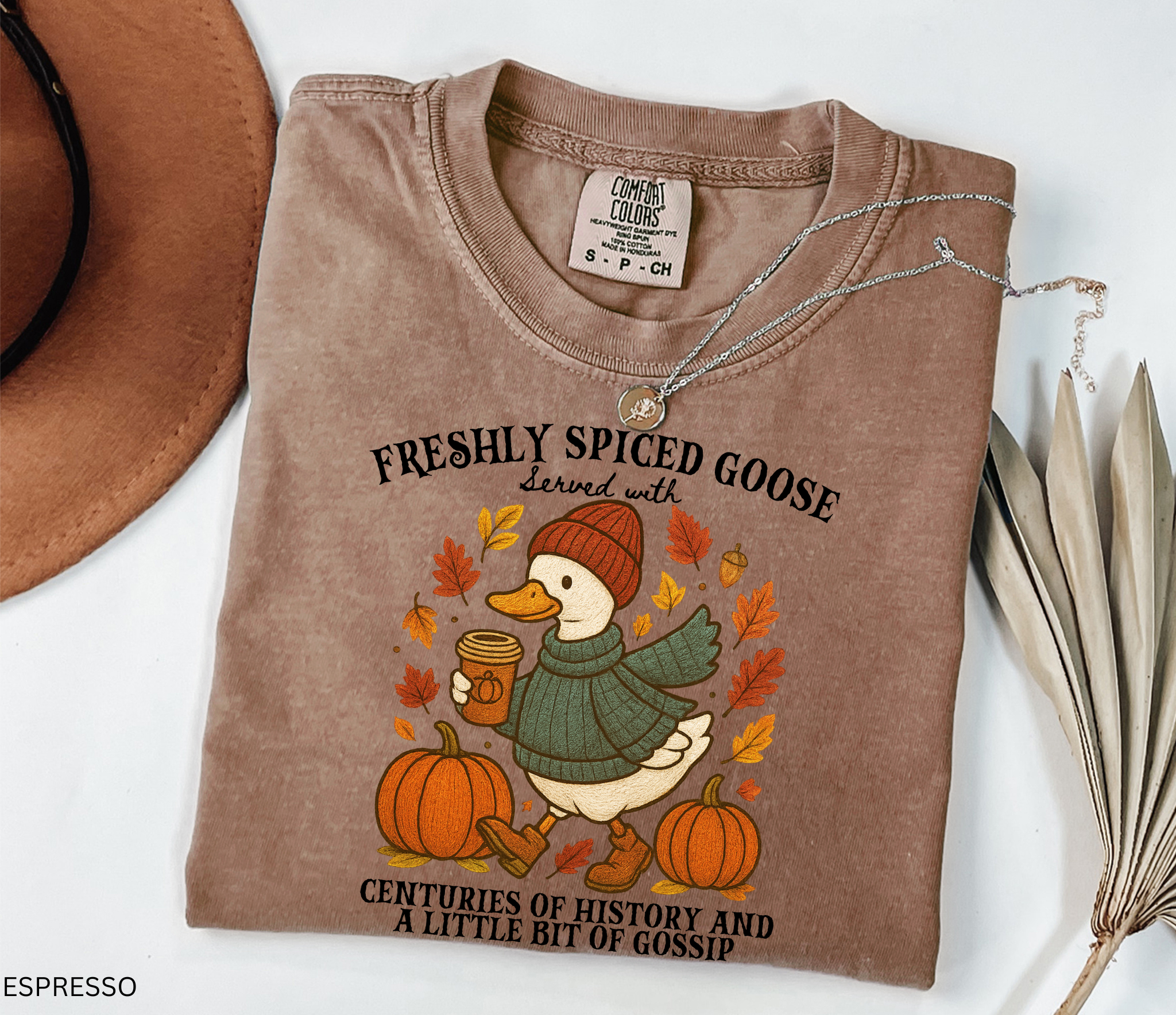 Cozy fall shirt design featuring a goose in a sweater and beanie holding pumpkin spice coffee, surrounded by pumpkins and autumn leaves – made for history teachers and professors.