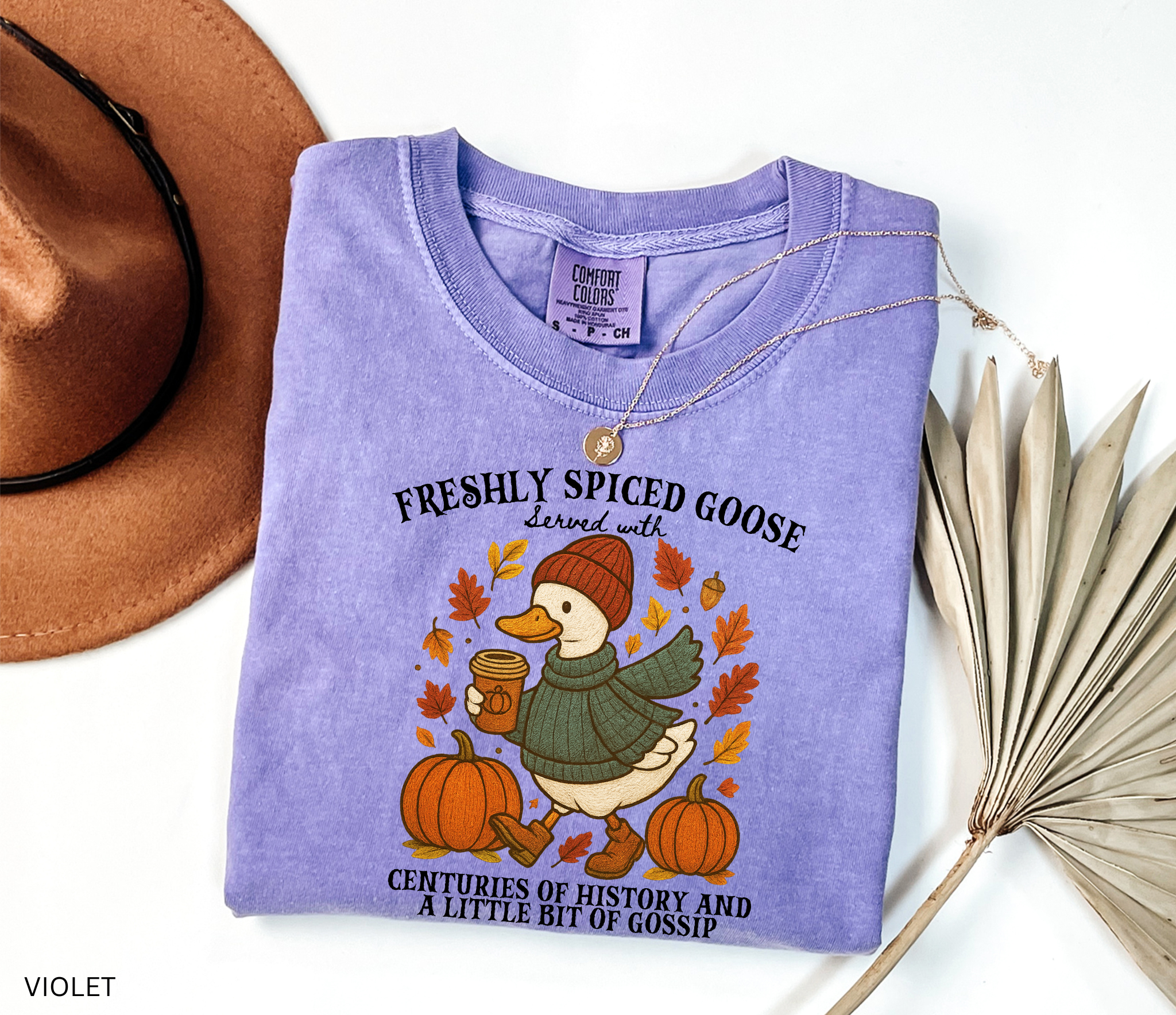 Cozy fall shirt design featuring a goose in a sweater and beanie holding pumpkin spice coffee, surrounded by pumpkins and autumn leaves – made for history teachers and professors.