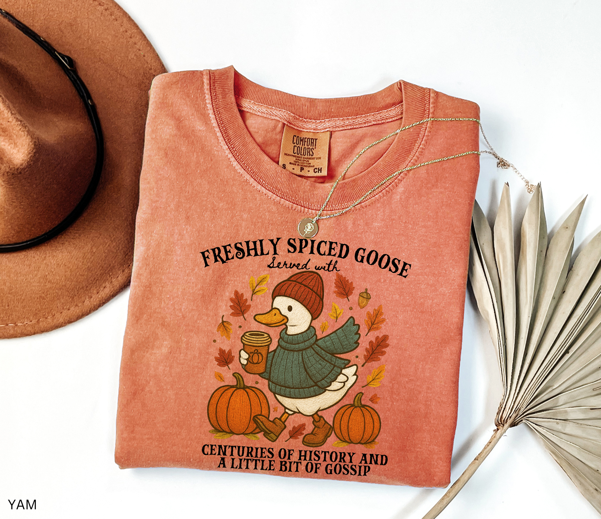 Cozy fall shirt design featuring a goose in a sweater and beanie holding pumpkin spice coffee, surrounded by pumpkins and autumn leaves – made for history teachers and professors.