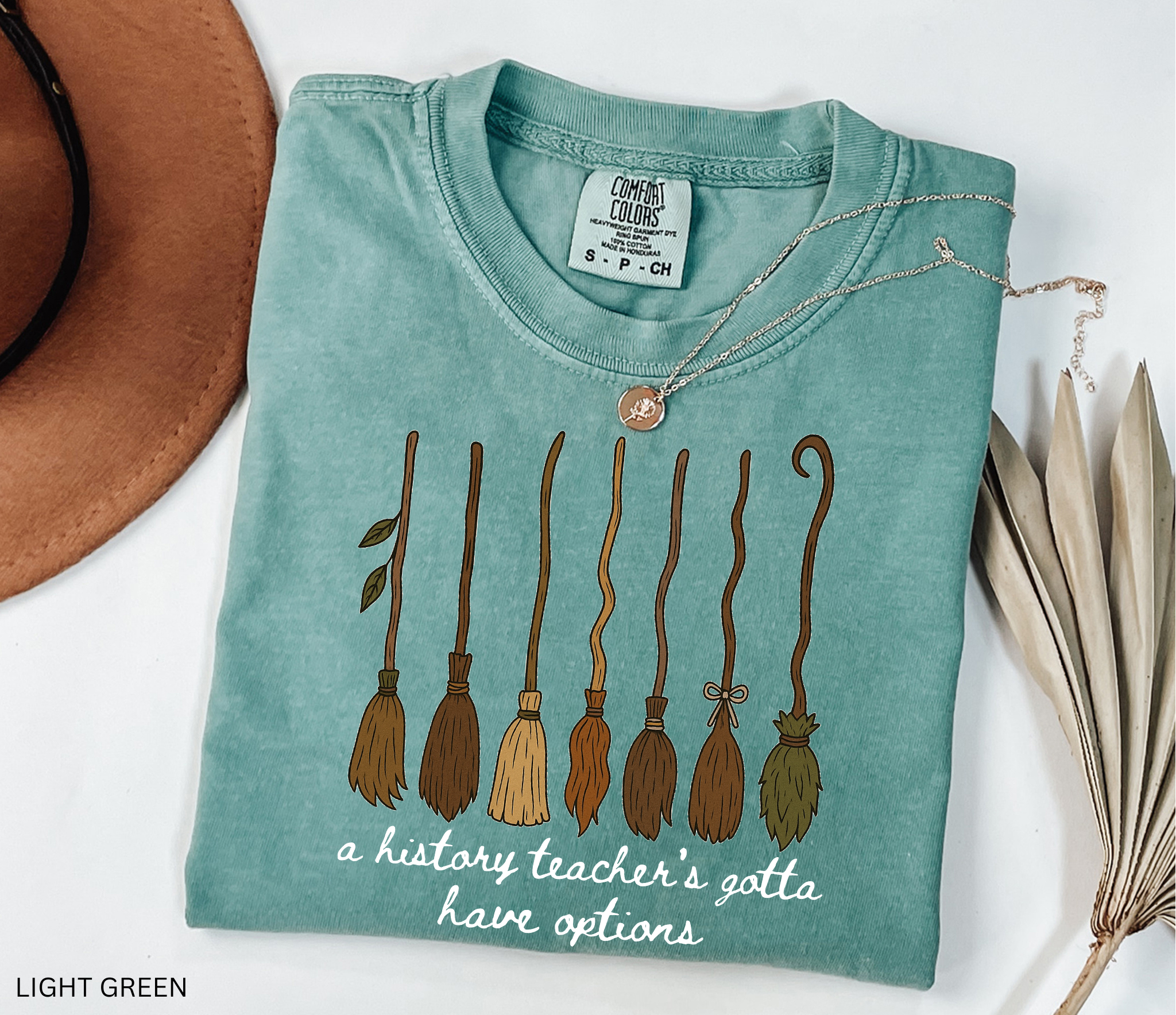 Halloween history teacher shirt featuring seven different broomsticks with the phrase “a history teacher’s gotta have options” in white script.
