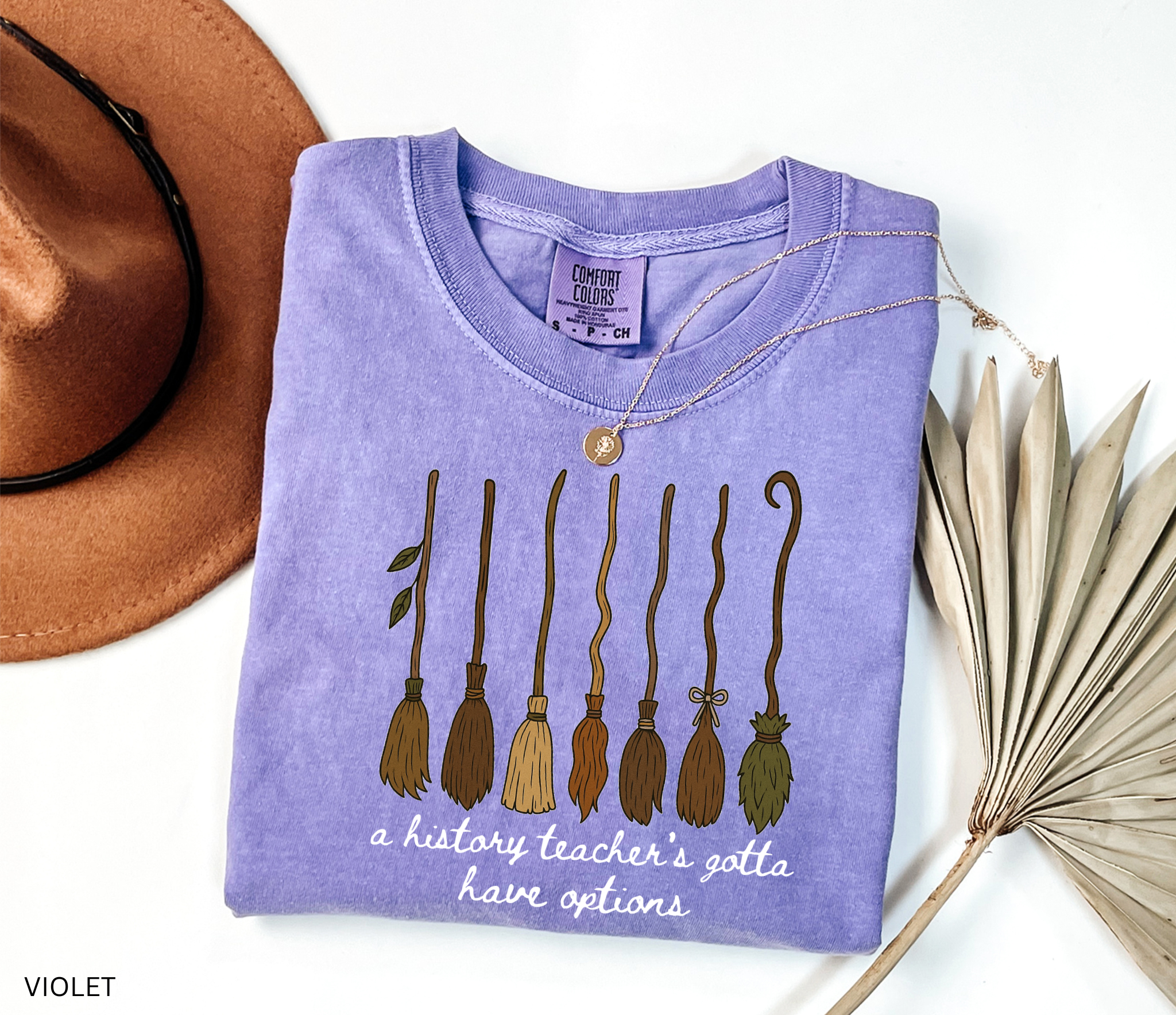 Halloween history teacher shirt featuring seven different broomsticks with the phrase “a history teacher’s gotta have options” in white script.