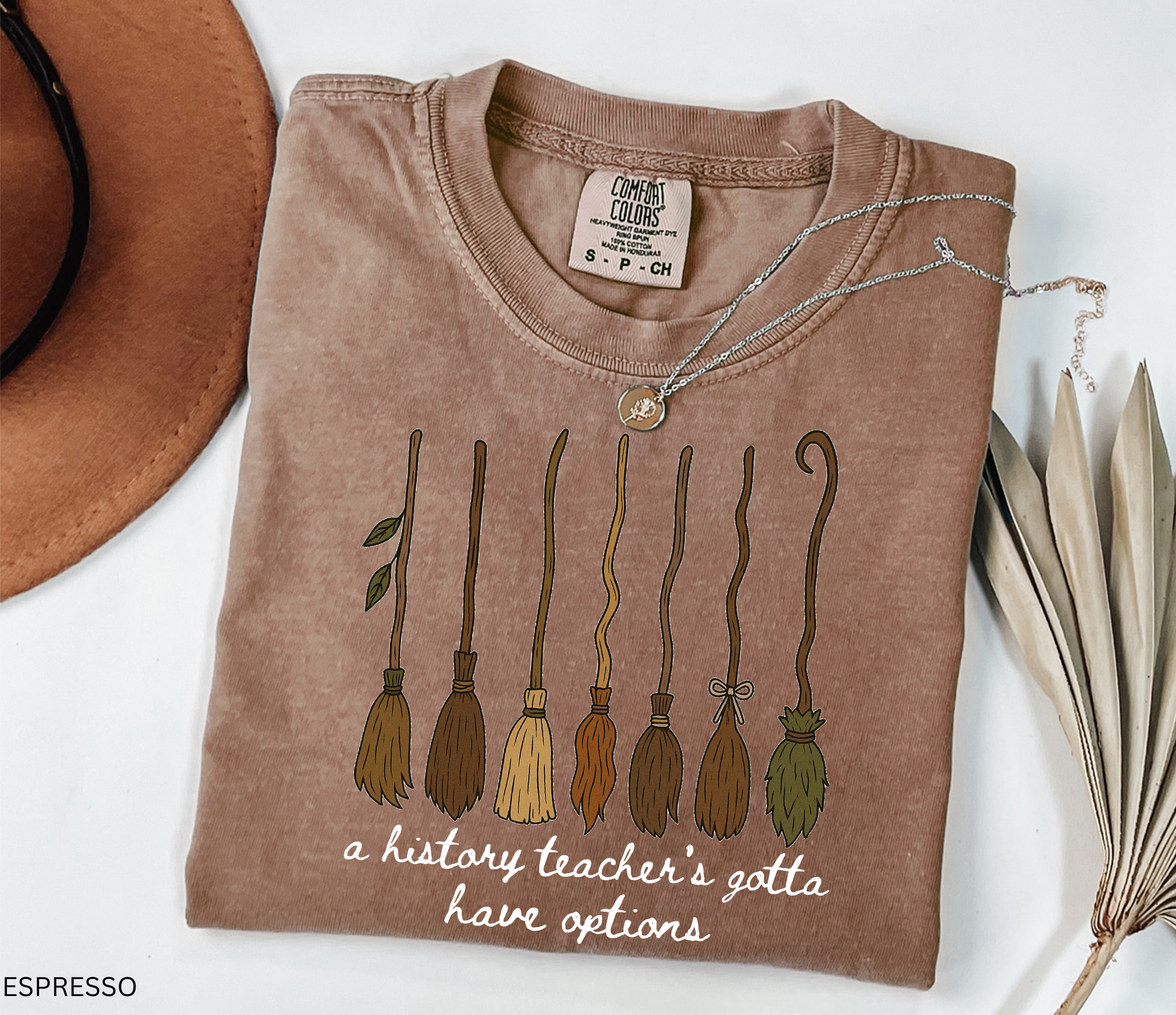 Halloween history teacher shirt featuring seven different broomsticks with the phrase “a history teacher’s gotta have options” in white script.