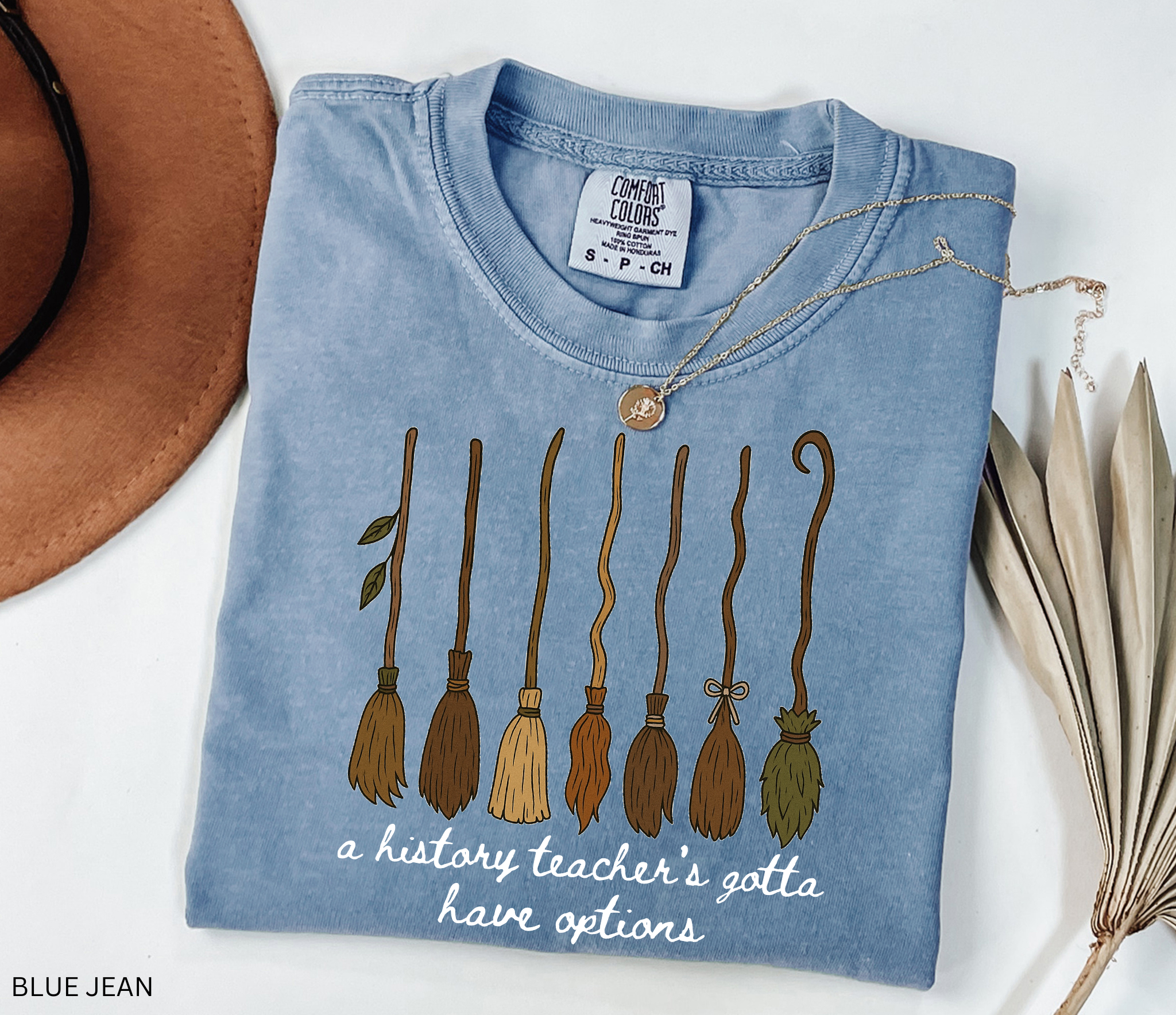 Halloween history teacher shirt featuring seven different broomsticks with the phrase “a history teacher’s gotta have options” in white script.